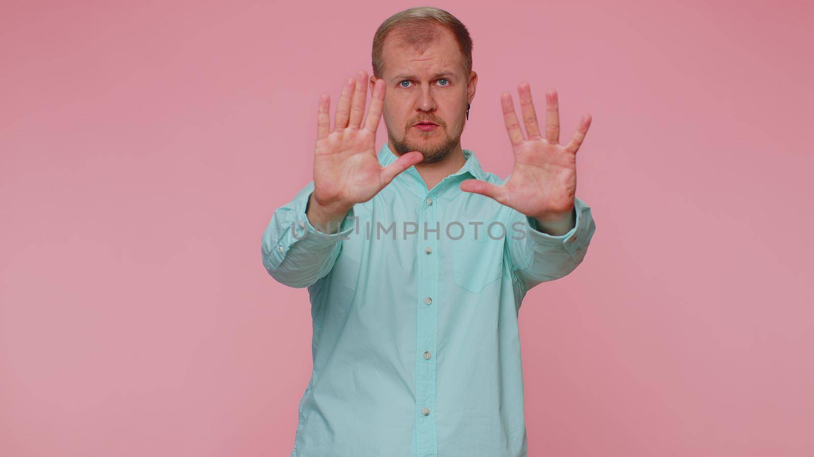No stop. Serious adult man say no, hold palm folded crossed hands in stop danger gesture, warning of finish, prohibited access, declining communication, body language. Young one guy on pink background