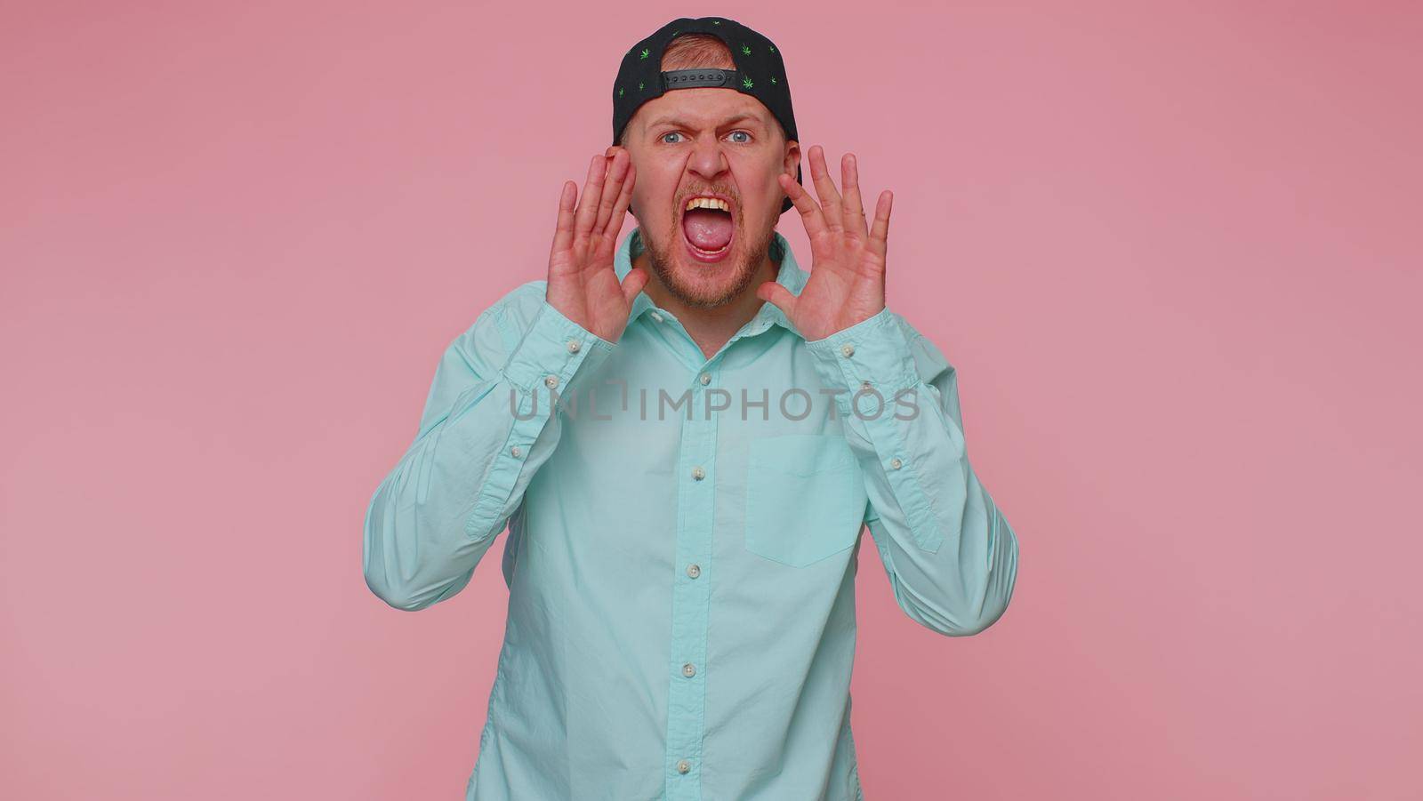 Expressive man holding hands near mouth loudly screaming, shouting, yelling, announces discounts sale Hurry up, welcomes someone hello. Young adult guy isolated alone on pink studio wall background