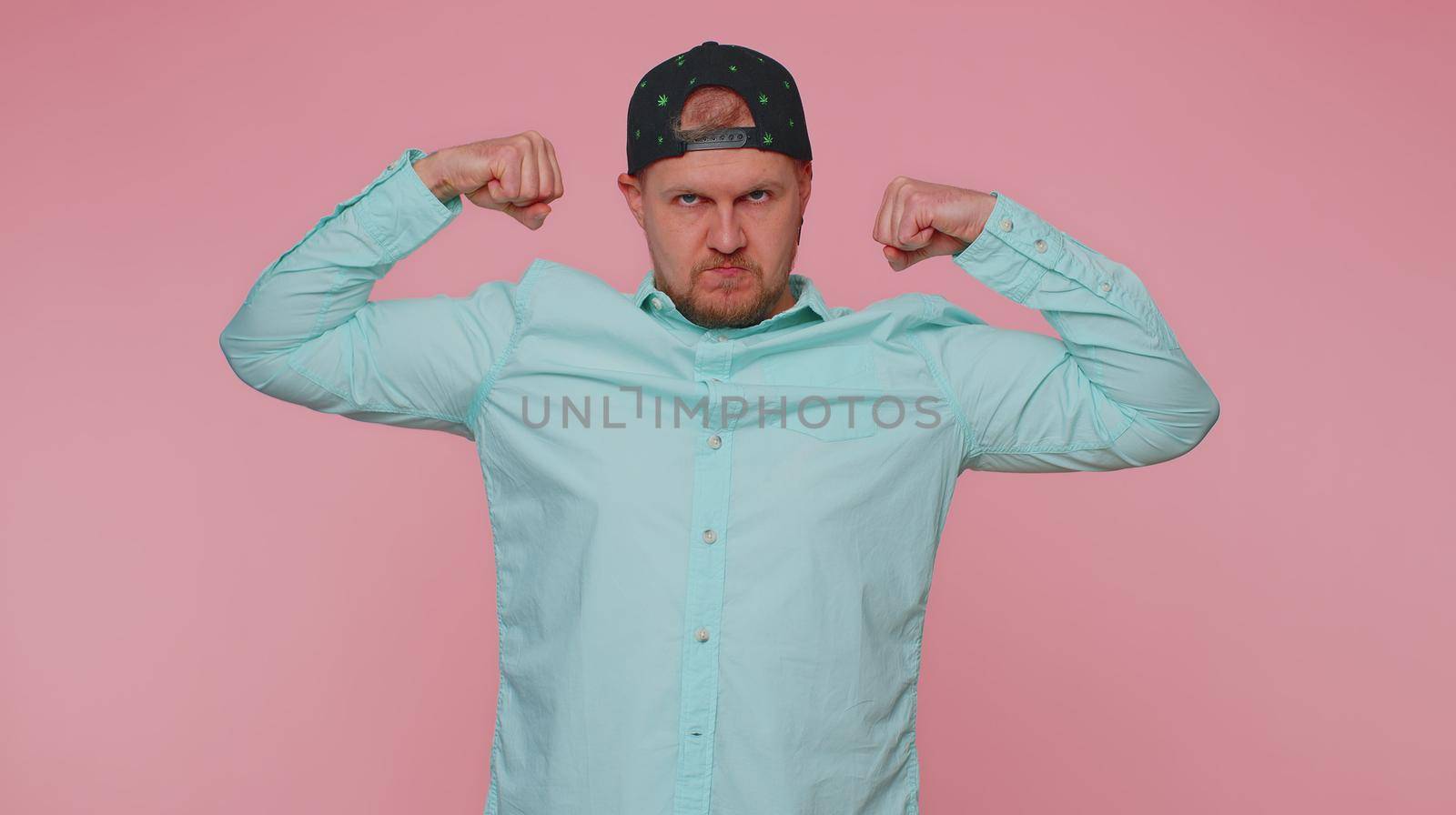 I am strong and independent. Man showing biceps and looking confident, feeling power strength to fight for rights, energy to gain success win. Young adult guy isolated on pink studio wall background