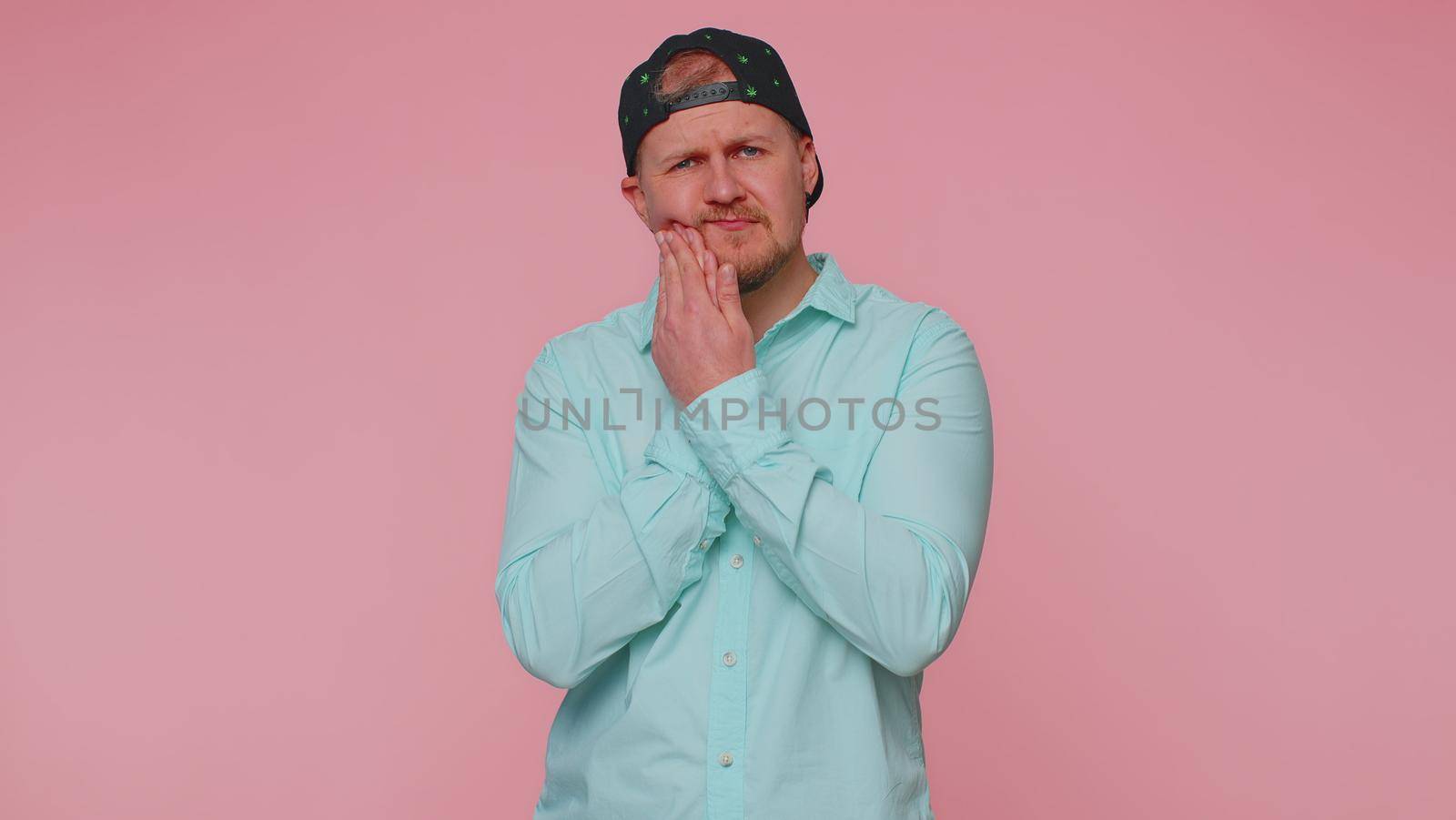 Bearded young man touching sore cheek suffering from toothache cavities or gingivitis waiting for dentist appointment, gums disease. Adult guy indoors studio shot isolated alone on pink background