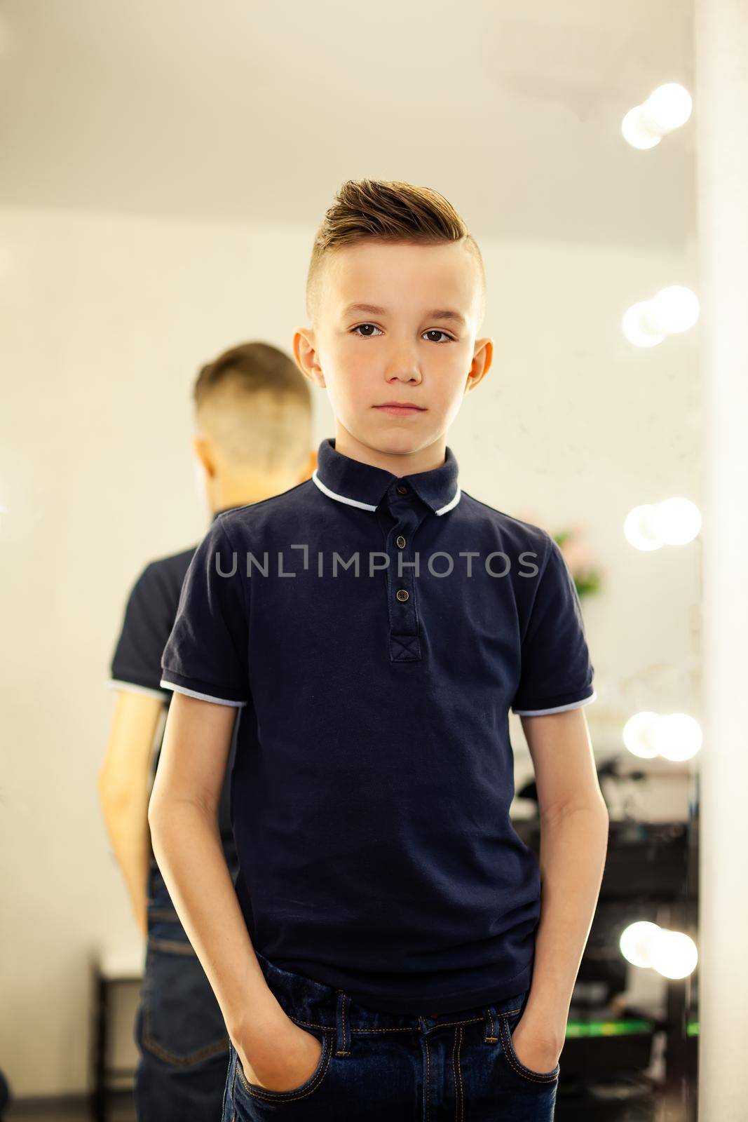 10-year-old boy in a hairdresser after a fashionable haircut in front of a mirror. A small child in a beauty salon looks at the camera posing. Hairdresser rape service.