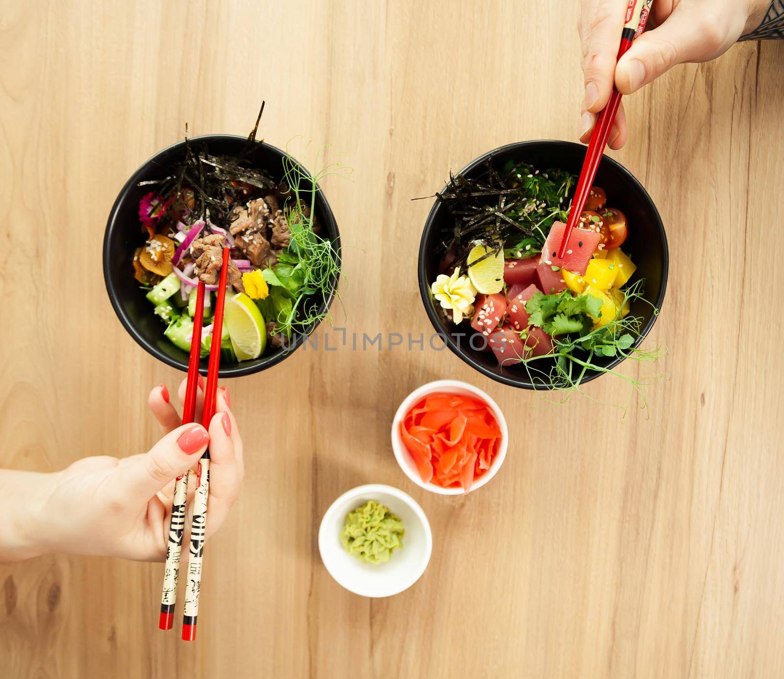 Man and woman eating poke salad with chopsticks. Dab tuna salad in a bowl. People in the restaurant eat salad with chopsticks. Asian seafood salad concept