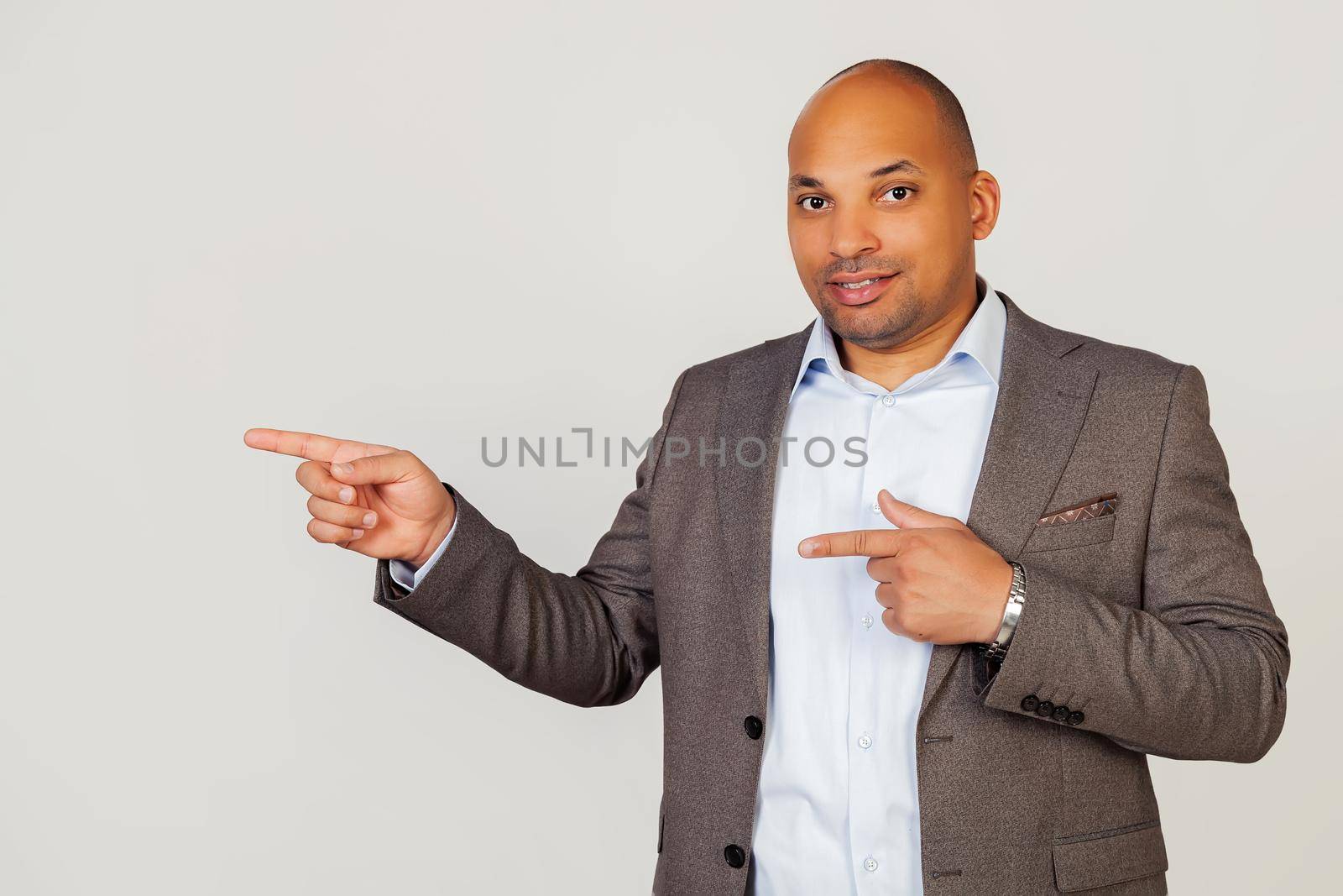 Happy young male African American businessman smiling happily and pointing to the side with index fingers on both hands while looking into the camera. Copy space for your ad