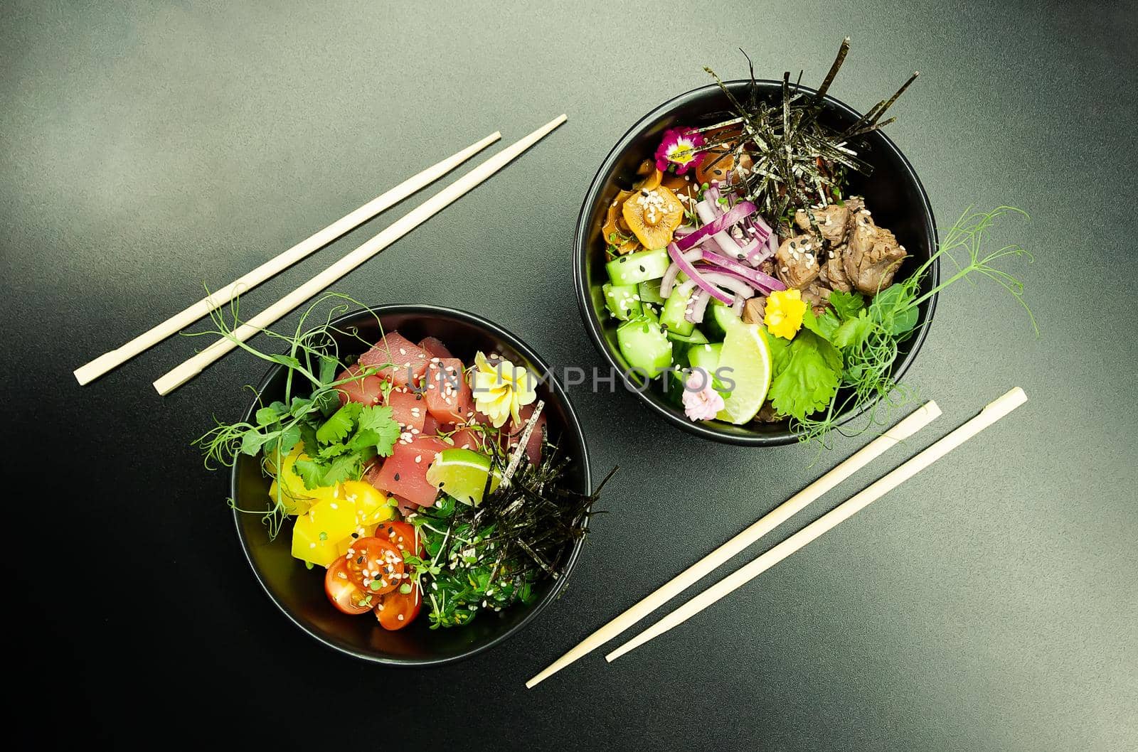 Poke salads with tuna and beef in bowls on the table. Two bowls of poke salad with chopsticks on a gray background. Asian seafood salad concept.