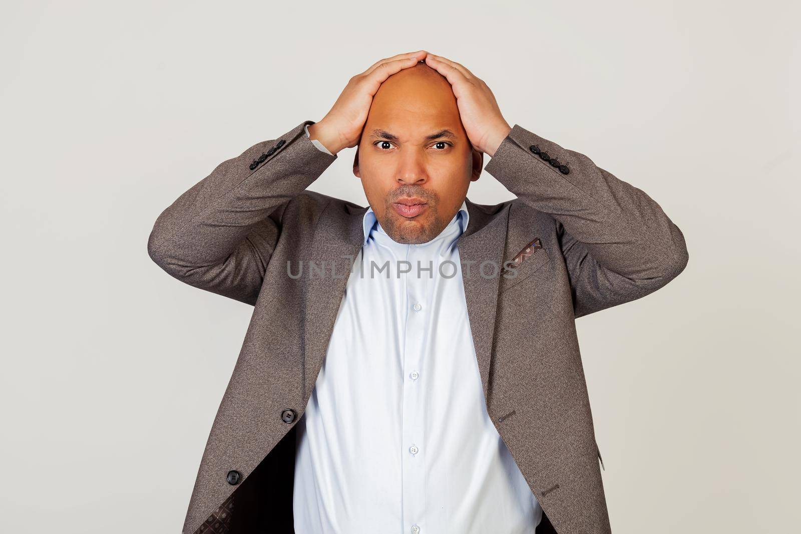 Upset shocked young African American guy businessman, holding hands on his head, was shocked by frowning and grabbing his head. Standing on a gray background