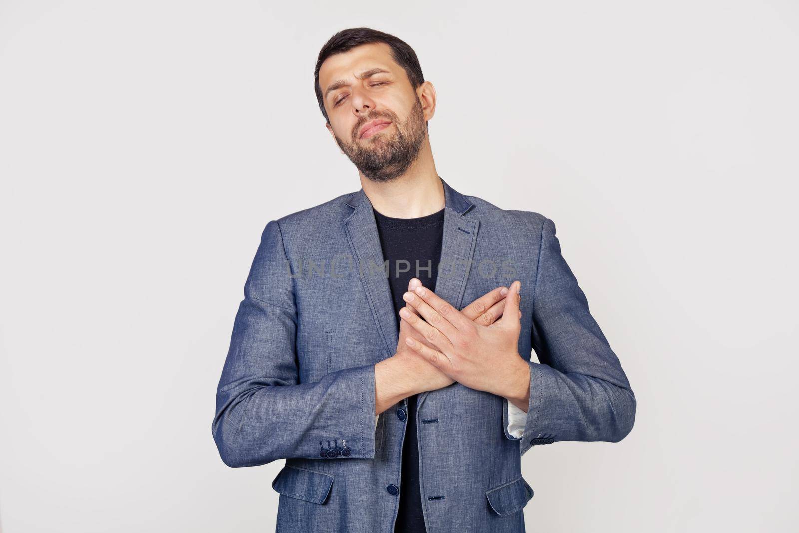 Young businessman with a smile man with a beard in a jacket, smiling with his hands on his chest with closed eyes and a grateful gesture on his face. Health concept.
