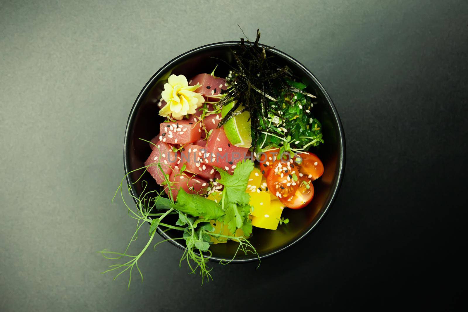 Poke salad with tuna in a bowl. Ingredients fresh tuna, cherry tomatoes, marinated seaweed, rice, takuan, Ponzu sauce, Teriyaki sauce, nori, sesame seeds, lime, cilantro. Asian seafood salad concept