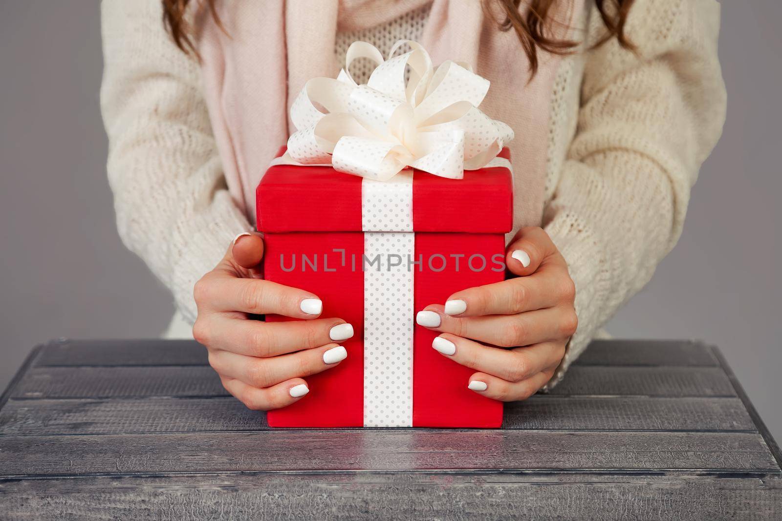 Female hands holding a red gift box with a white ribbon. Christmas gift box on a gray background. Girl holding Christmas shopping, greets New Year. Shopping sale concept