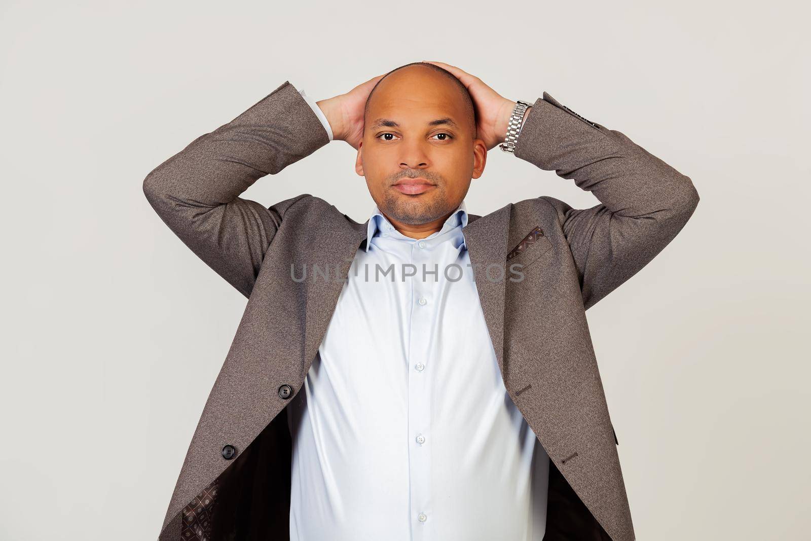 Portrait of a tired young African American guy businessman looking at the camera holding his hands behind his head, leaning back in a chair to rest a few minutes on a hard day in the office.