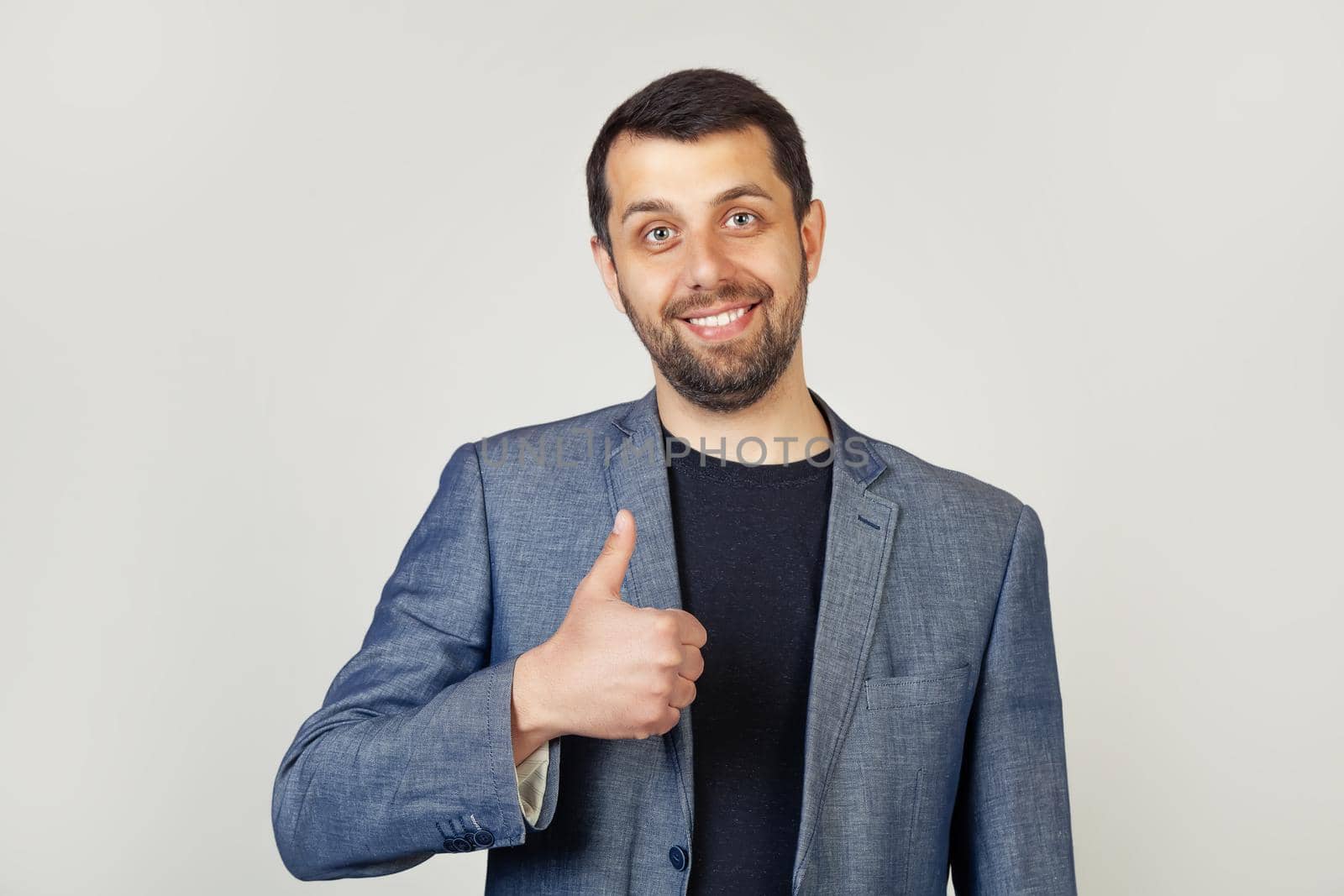 Young man with bristle businessman showing finger up to camera with a happy smile. All is well, shows success.