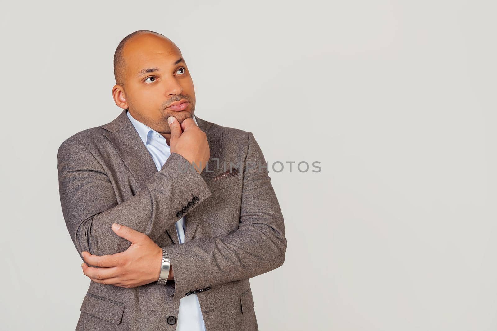 Handsome young male African American businessman in jacket looking to the side and thinking touching chin with hand looking to the side with pensive facial expression. by ViShark