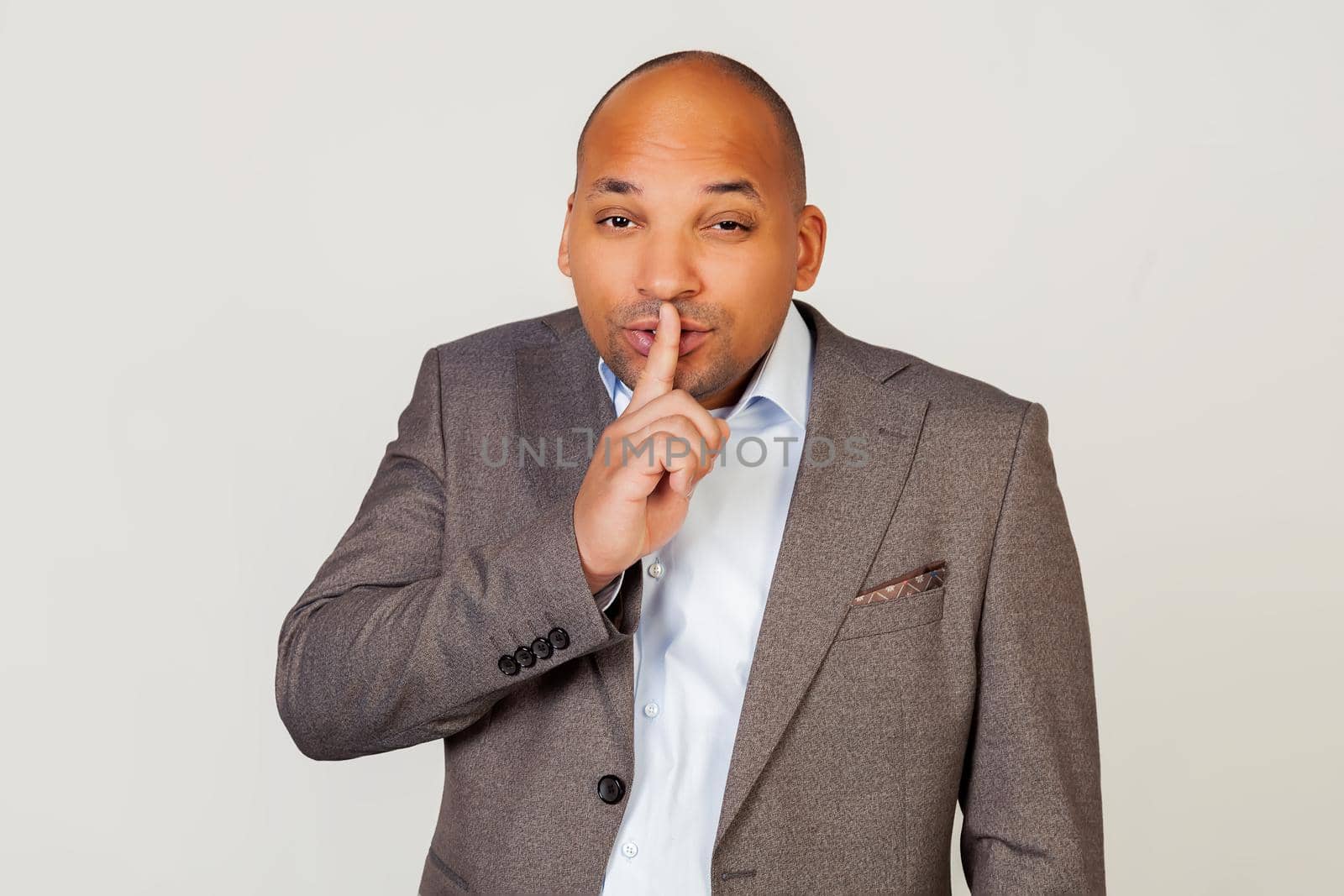 Man african american businessman in a jacket makes a gesture with his hand holding a finger on his lips, asks for silence and silence.