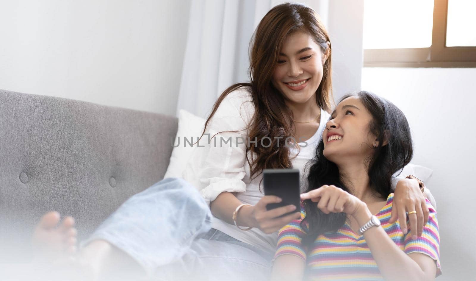 Young beautiful Asian women lesbian couple lover using smartphone video call online in living room on sofa at home with smiling face.Concept of LGBT sexuality with happy lifestyle together. by wichayada