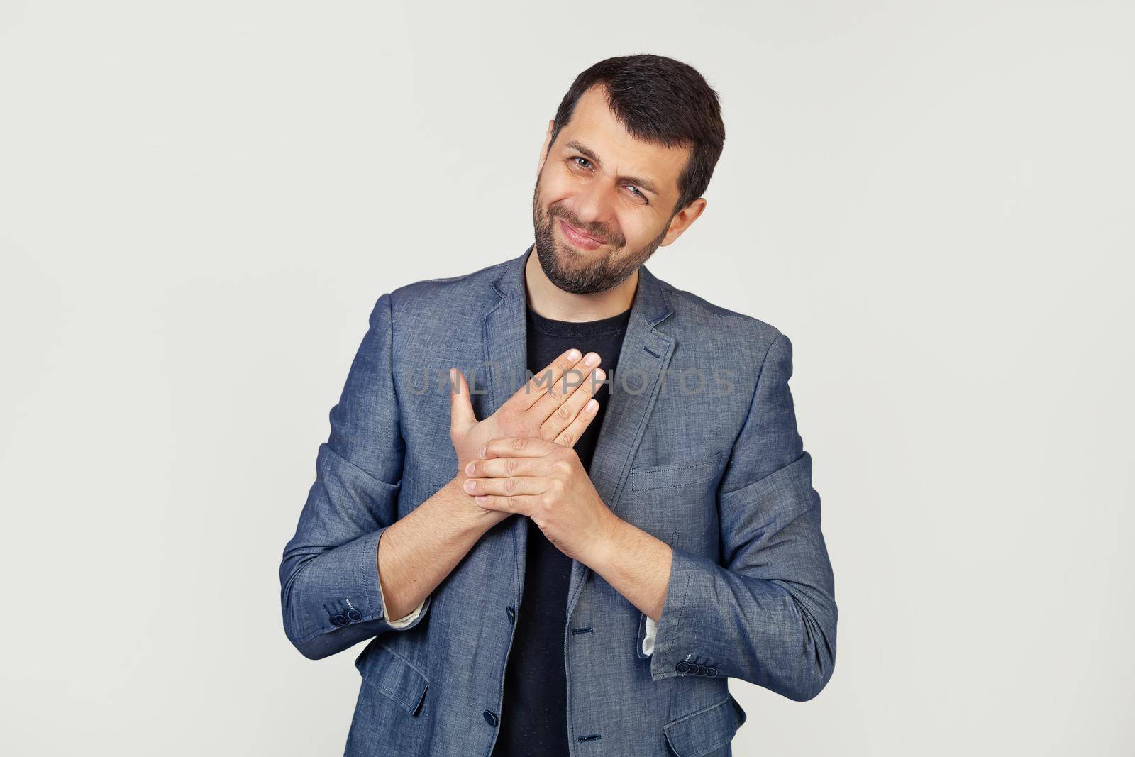 Young businessman man with a beard in a jacket, suffering from pain in the hands and fingers, inflammation of arthritis. Portrait of a man on a gray background.