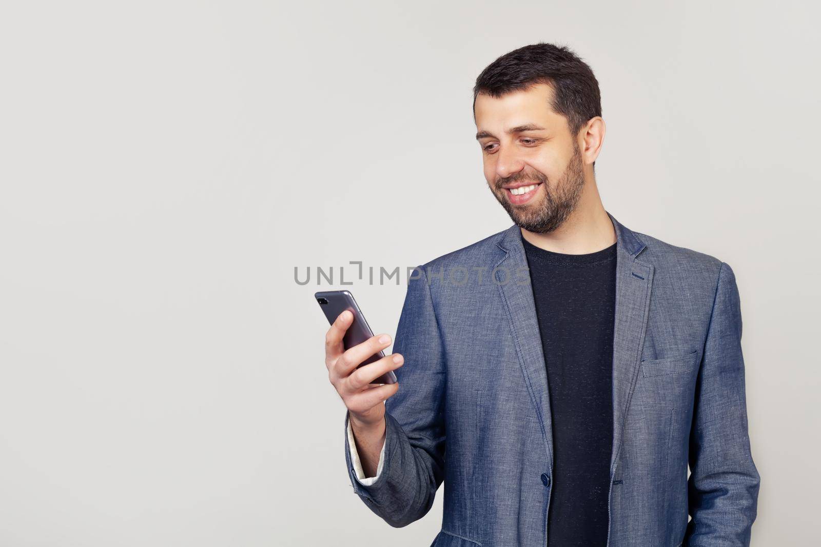 Portrait of a young male entrepreneur with a beard, modern, having a smartphone in his hands, busy checking e-mail, reading a message in the messenger, browsing or sending SMS using 5G, Wi-Fi