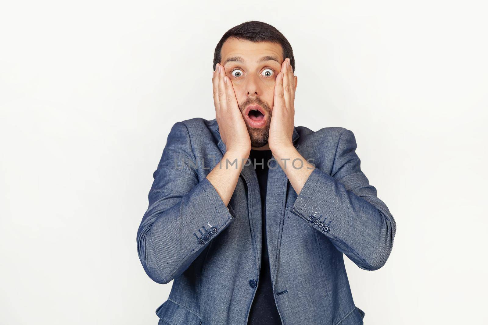 Young businessman man with a beard scared and shocked, surprised and surprised with hands on his face. Portrait of a man on a gray background.