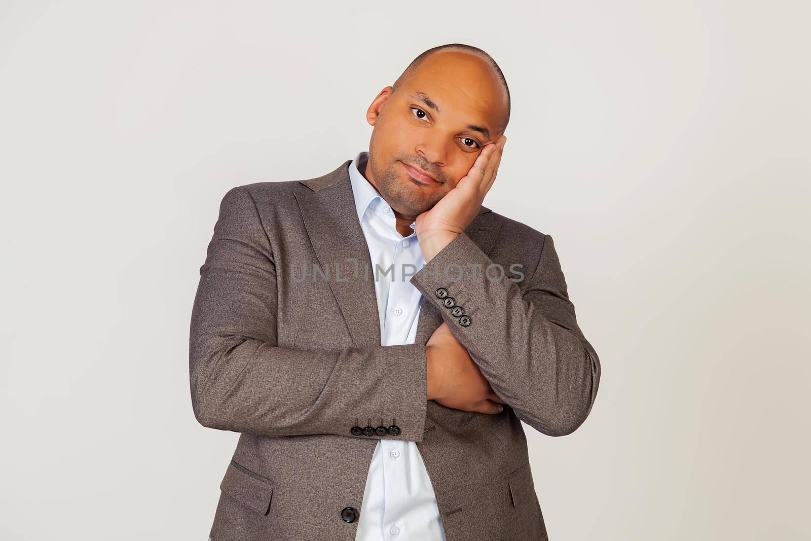 Portrait of a young african american guy businessman holding his hand on his face and staring indifferently at the camera, thinks he looks tired and depressed with crossed arms. gray background.