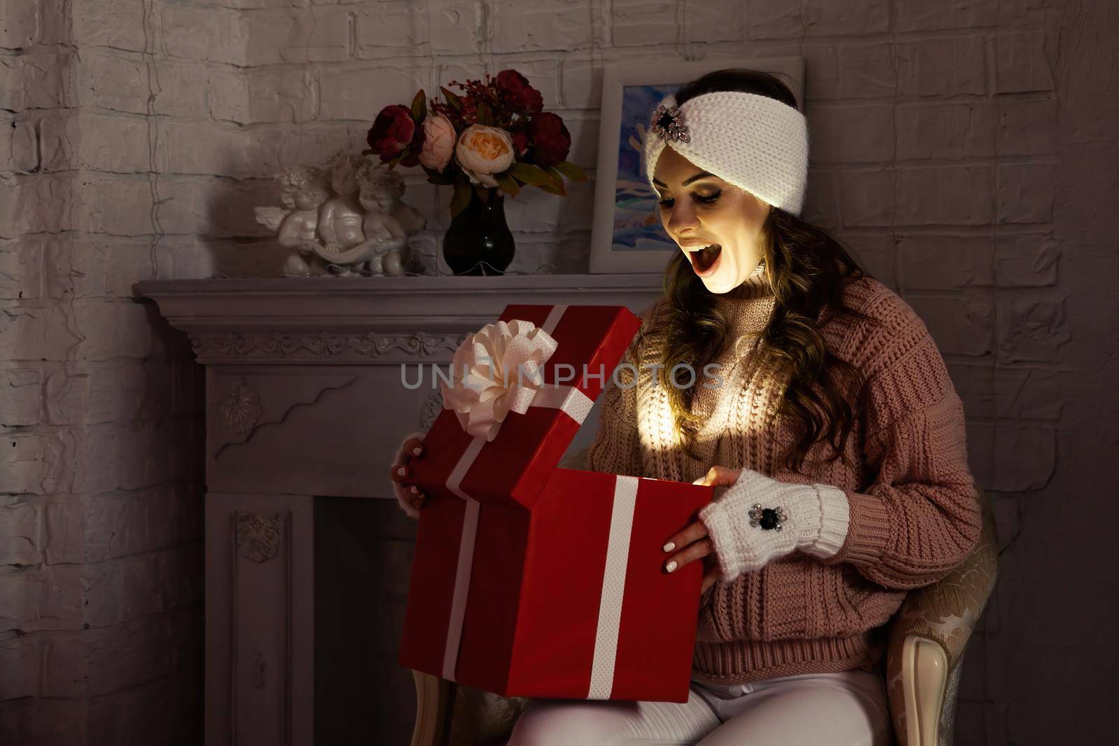 Happy young woman with a present, opening a Christmas present box. Portrait of happy smiling girl opening gift box isolated on red background