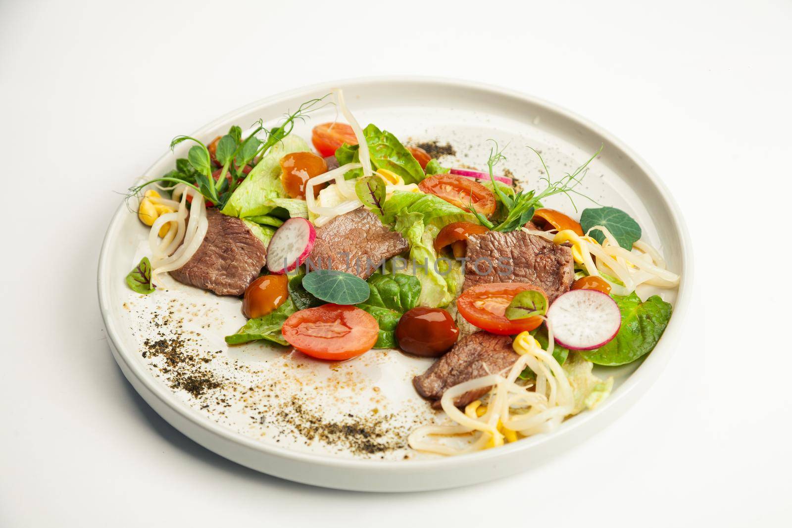 Salad with beef tataki on a plate. Ingredients Iceberg lettuce, tataki beef, nameko mushrooms, cherry tomatoes, moashi, spinach, ponzu sauce. For restaurant menu.