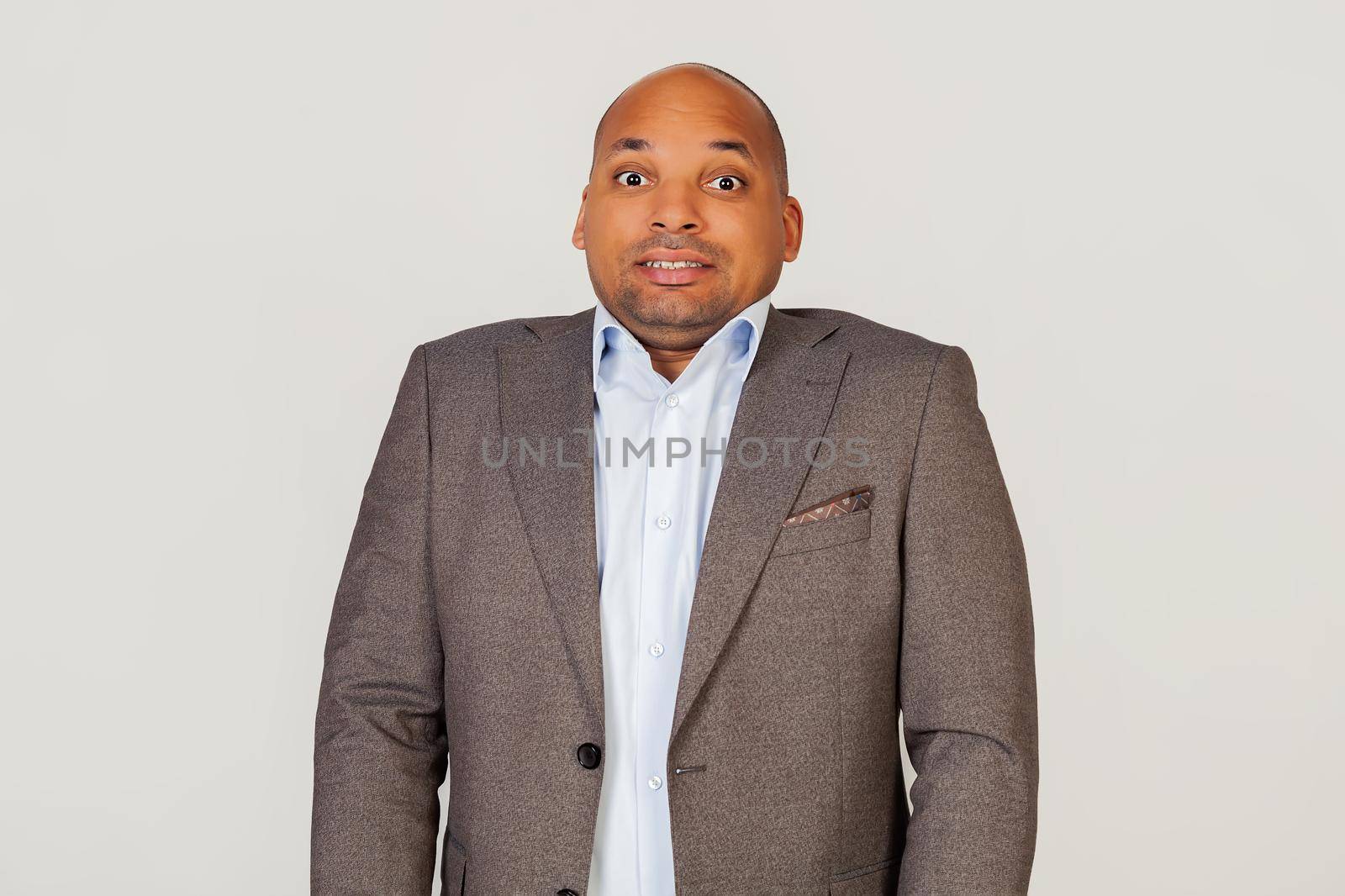 Annoyed African American guy businessman frowns with displeasure, annoyed with bad news, feeling disgusted and displeased, looks excited, gesturing funny and comical. Standing on a gray background