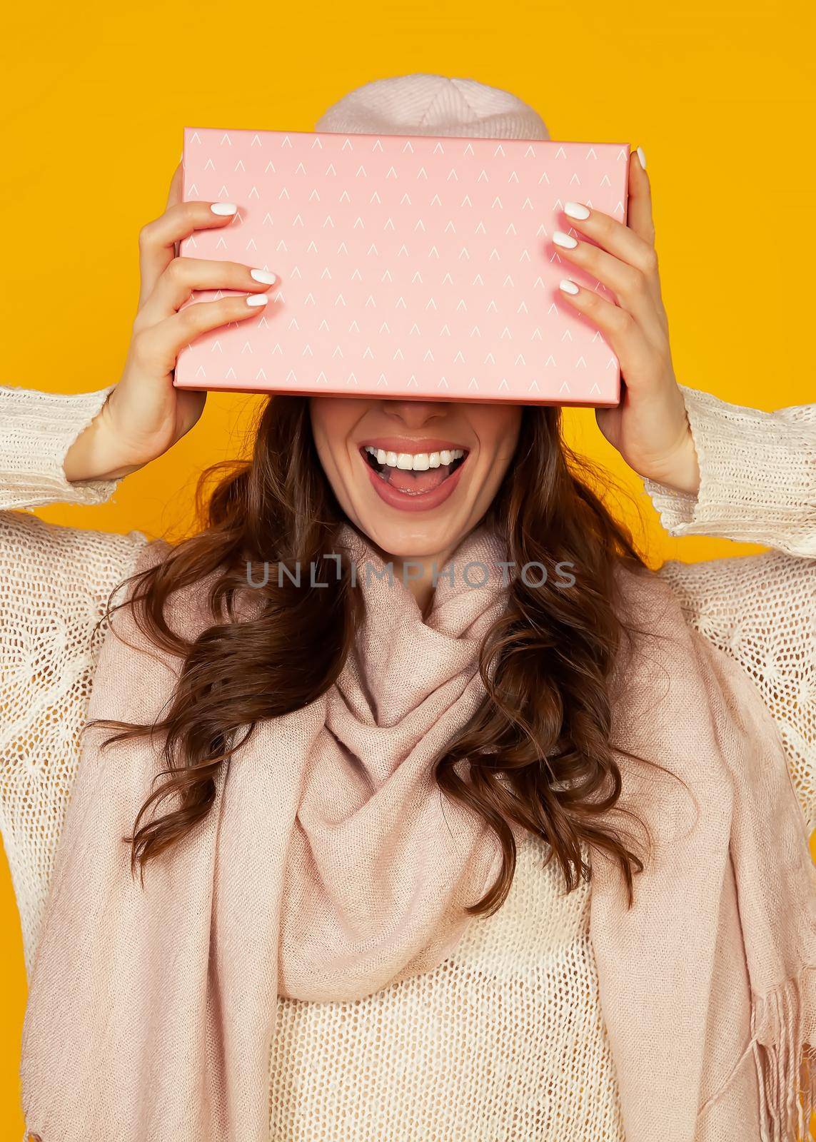 Happy young woman with a gift box in her hands, covers half of her face with a New Year's gift. The girl shows a gift to the camera. The concept of gifts and surprises for the new year and christmas.