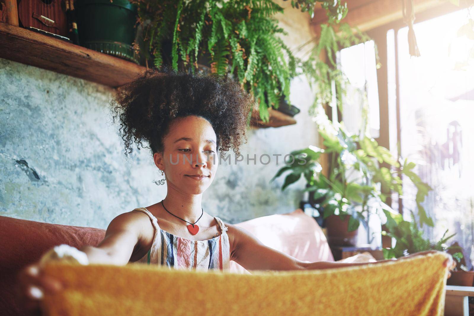 Shot of a beautiful African woman folding washed laundry while sitting on her couch - Stock Photo