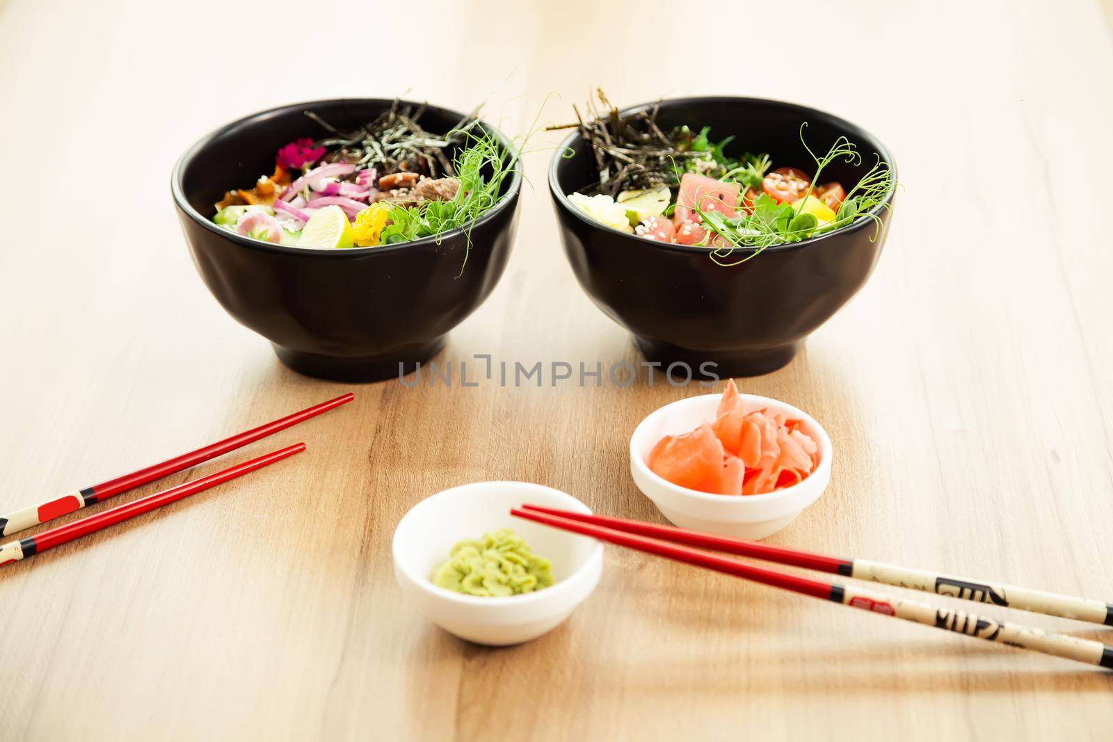 Two poke salads with beef and tuna in a bowl with various sauces on the restaurant table. Poke salads in a bowl next to chopsticks and ginger with wasabi. Asian salad concept.