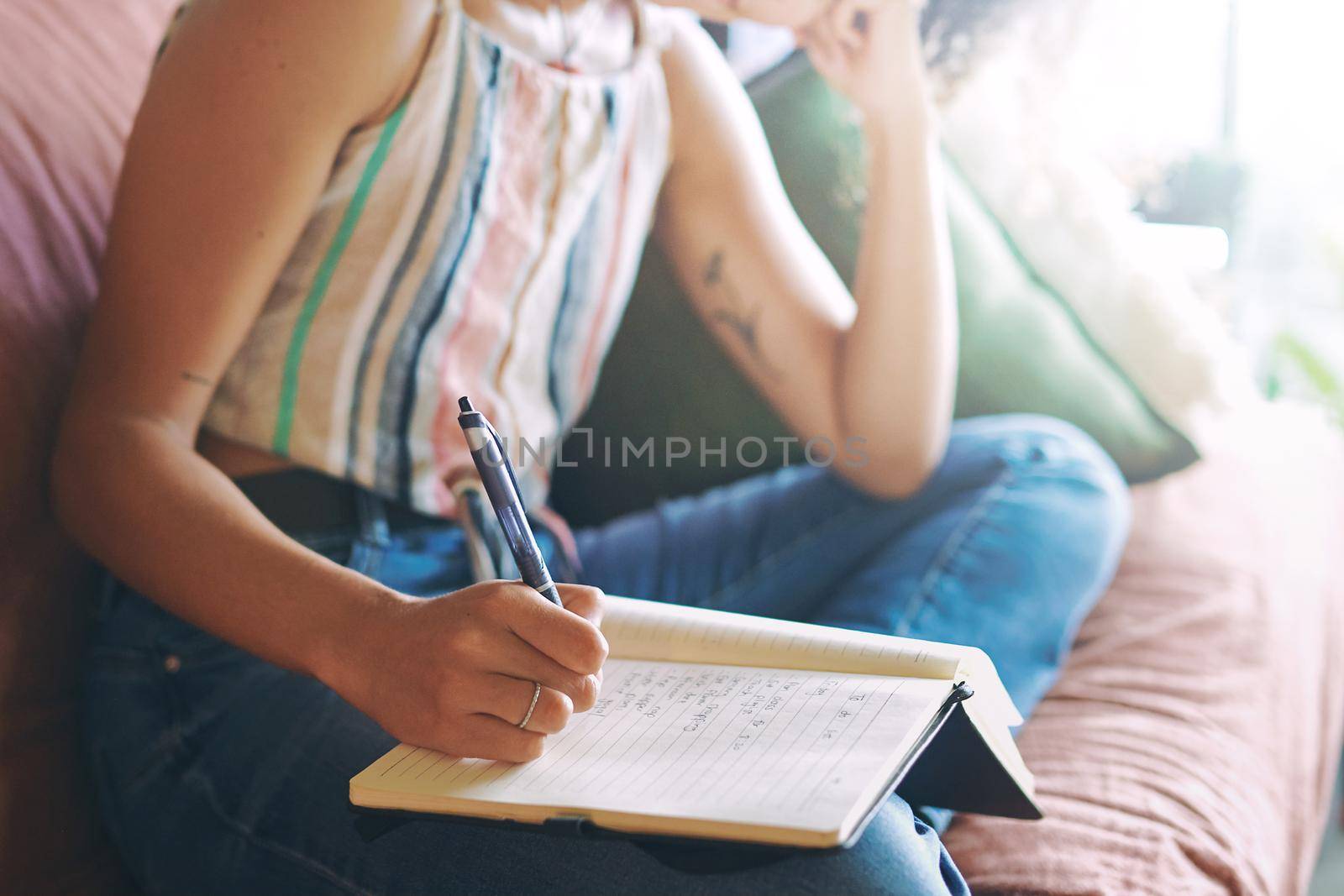 Shot of a unrecognizable woman making notes while relaxing on the sofa at home stock photo