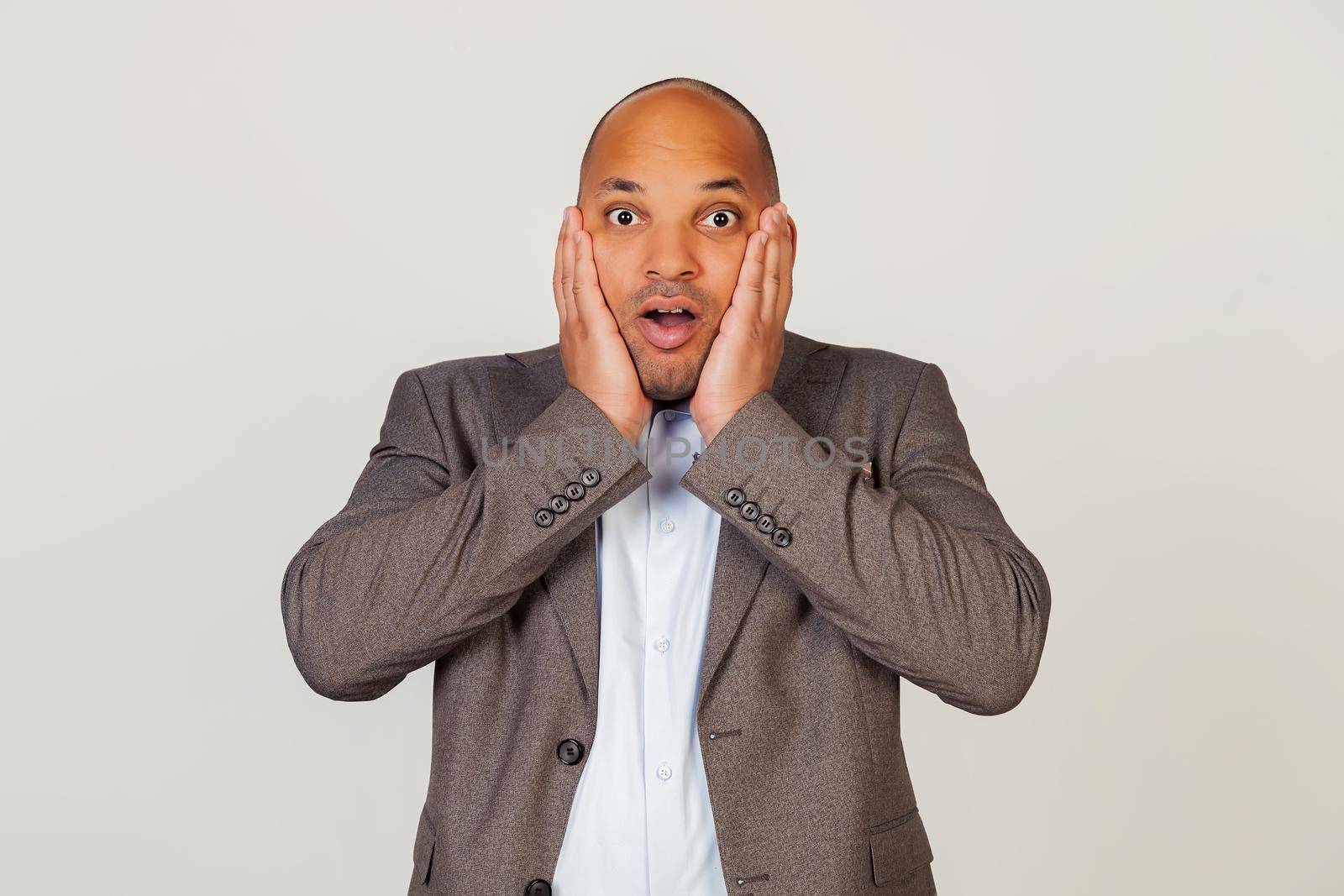 Shocked young african american guy businessman expressing surprise and amazement, touching his face and folding his lips, stands in a stupor and goggles at the camera, being impressed