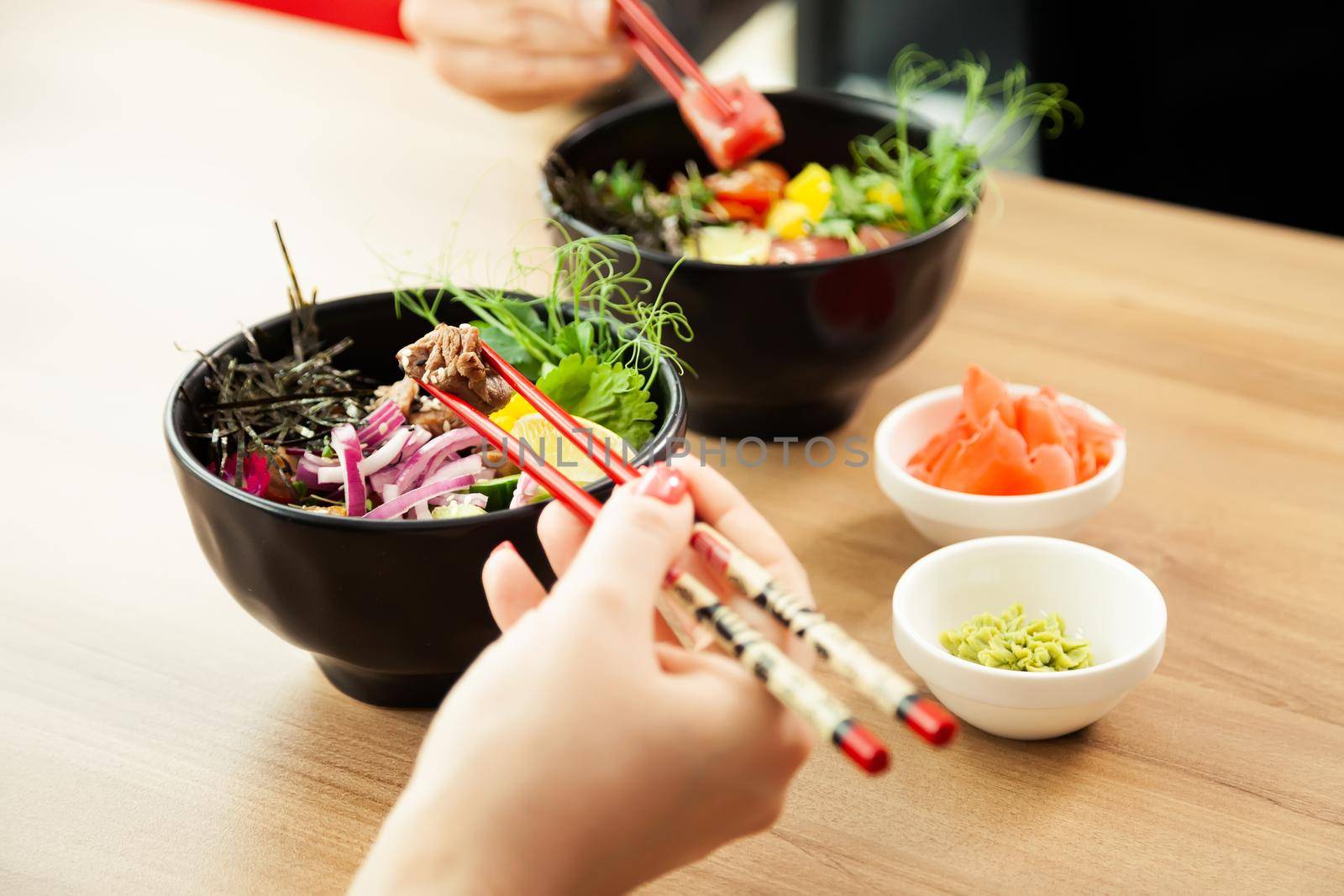 Man and woman eating poke salad with chopsticks. Dab tuna salad in a bowl. People in the restaurant eat salad with chopsticks. Asian seafood salad concept