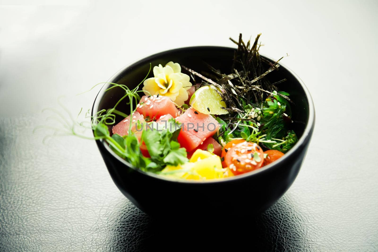 Poke salad with tuna in a bowl. Ingredients fresh tuna, cherry tomatoes, marinated seaweed, rice, takuan, Ponzu sauce, Teriyaki sauce, nori, sesame seeds, lime, cilantro. Asian seafood salad concept