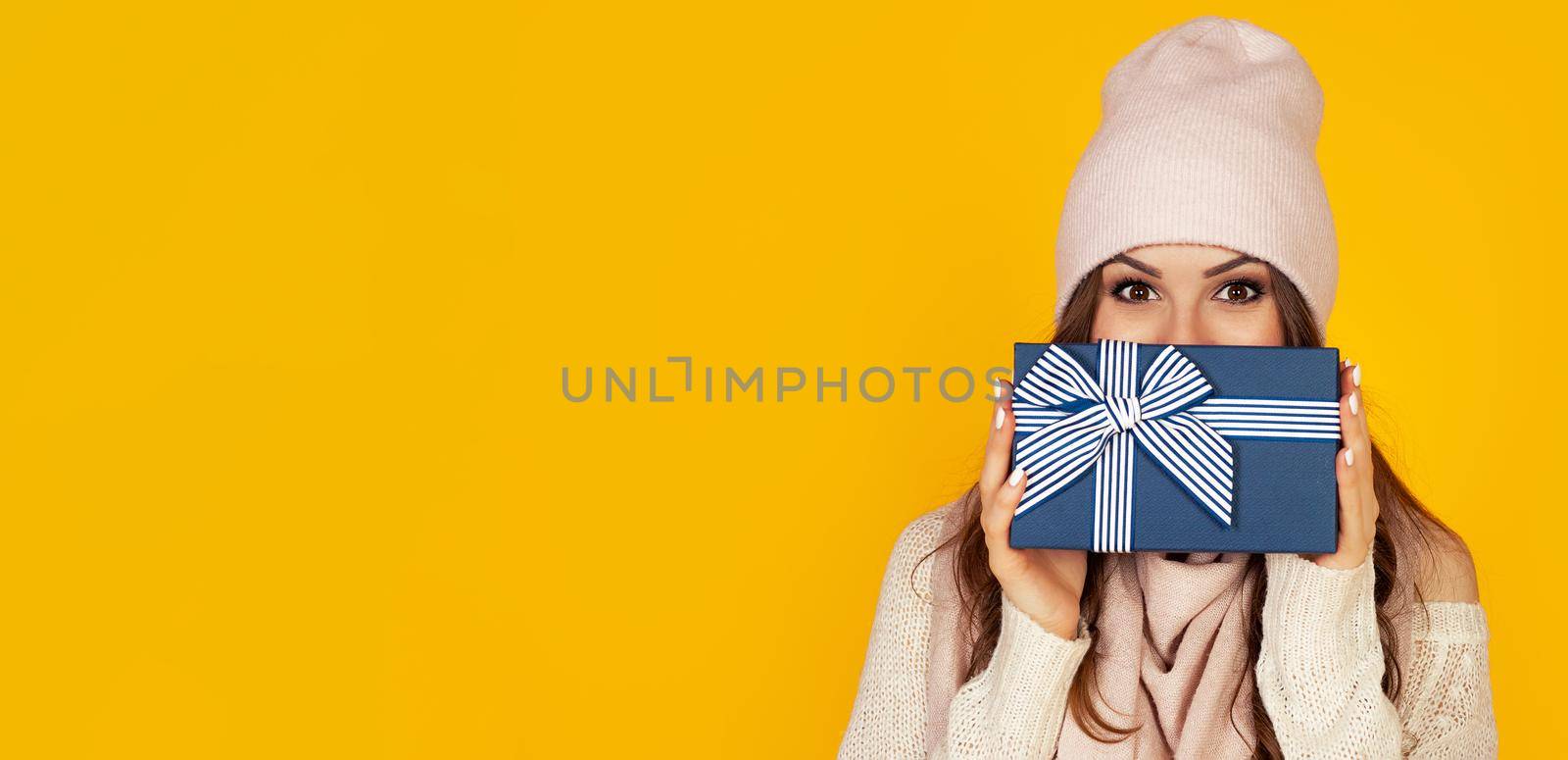 Happy young woman with a gift box in her hands, covers half of her face with a New Year's gift. The girl shows a gift to the camera. The concept of gifts and surprises for the new year and christmas.