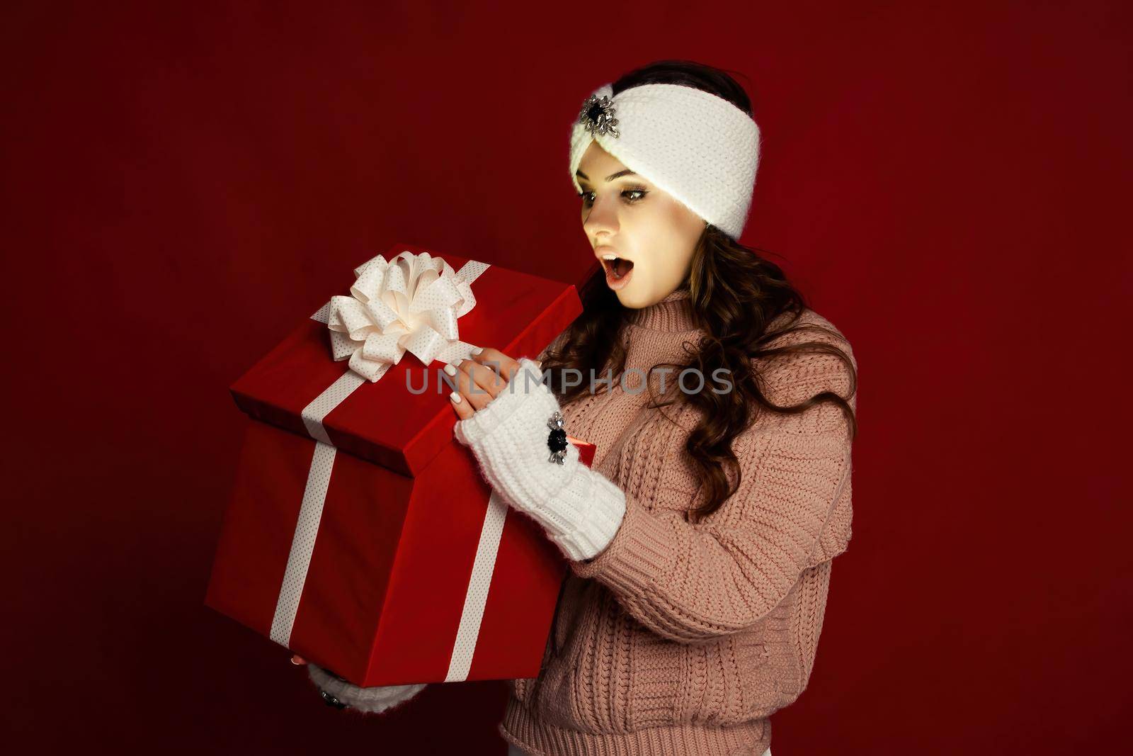 Happy young woman with a present, opening a Christmas present box. Portrait of happy smiling girl opening gift box isolated on red background