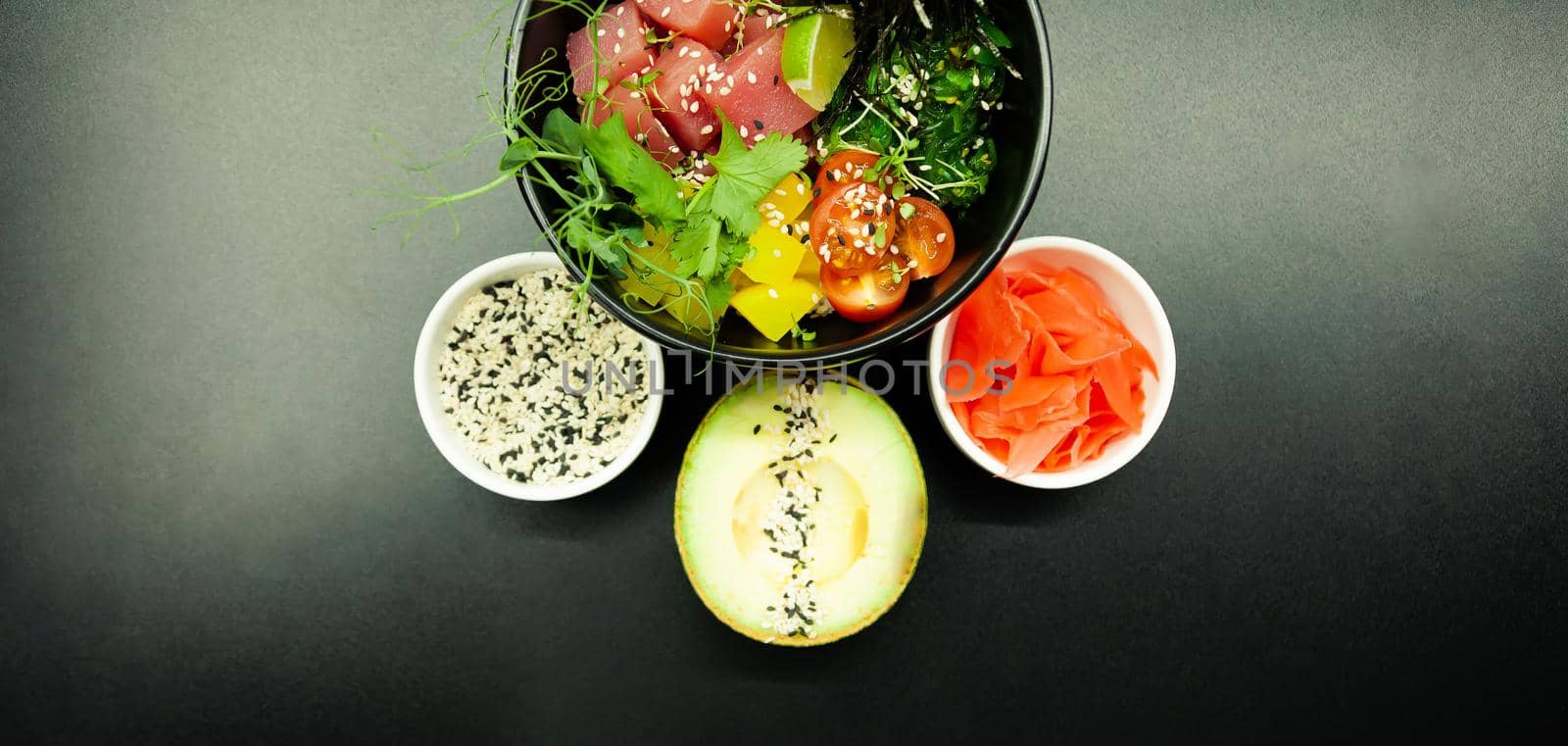 Poke salad with tuna in a bowl. Ingredients fresh tuna, cherry tomatoes, marinated seaweed, rice, takuan, Ponzu sauce, Teriyaki sauce, nori, sesame seeds, lime, cilantro. Asian seafood salad concept