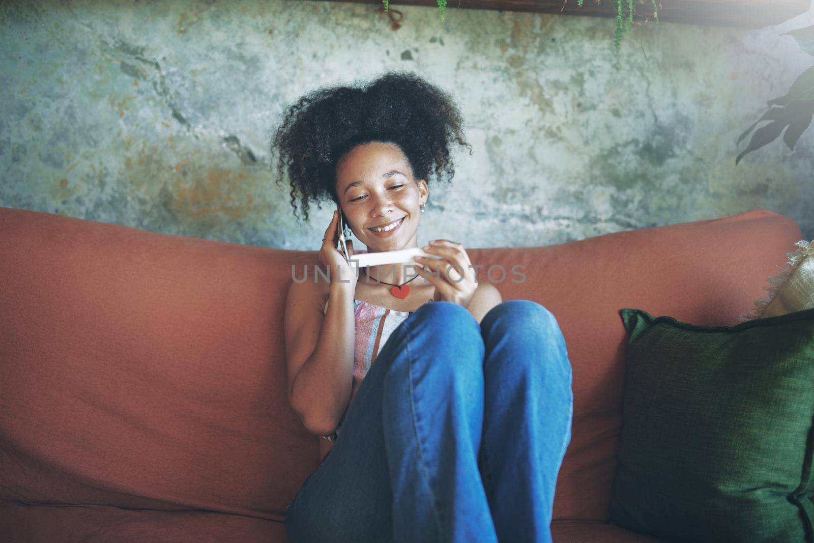 Shot of a young woman taking a pregnancy test on her sofa while talking on her smartphone