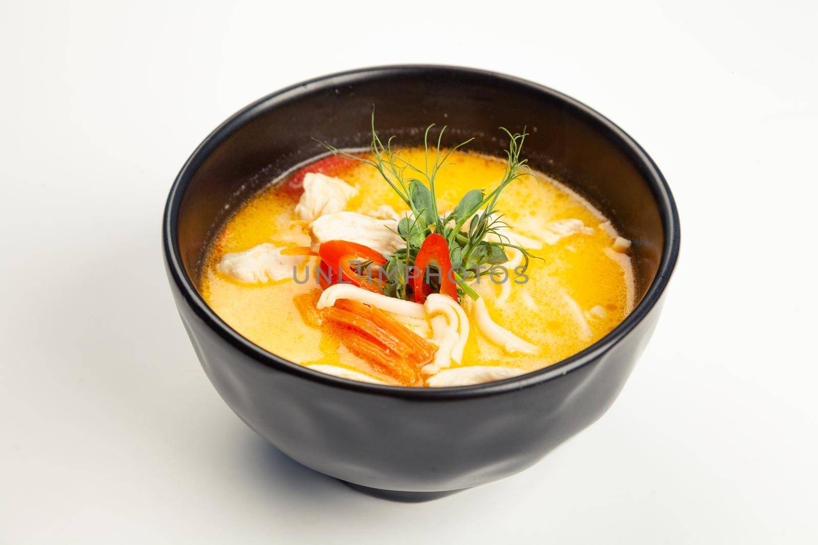 Soup with chicken and coconut milk in a black karelian. Ingredients broth, chicken fillet, coconut cream, Udon noodles, Bulgarian pepper, carrots, vegetable oil, chili pepper, salt. For restaurant menu.