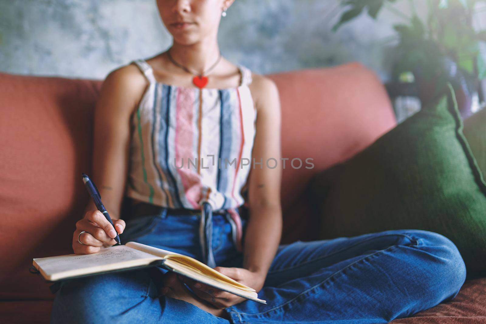 Shot of a unrecognizable woman making notes while relaxing on the sofa at home stock photo