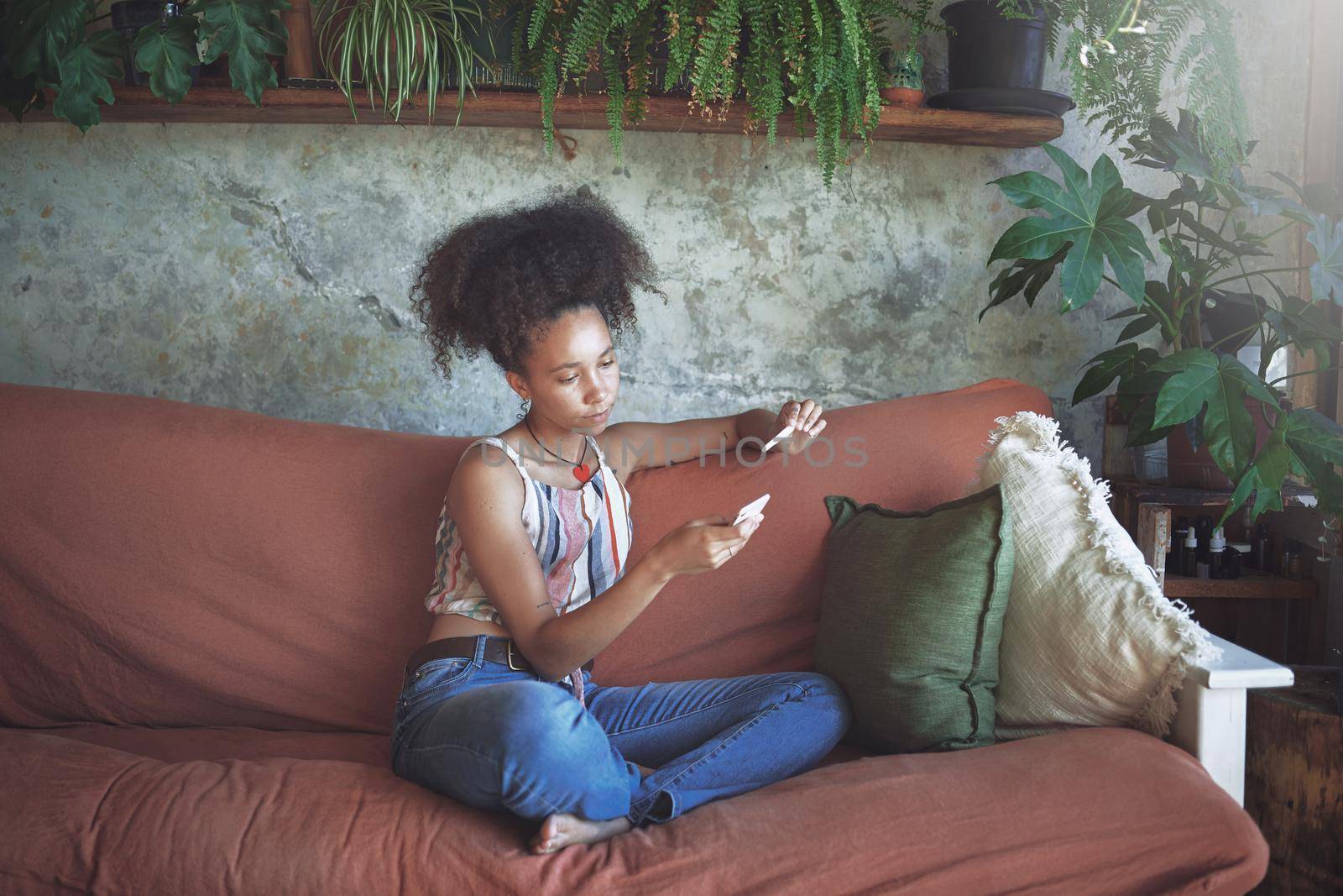 Shot of a young woman taking a pregnancy test on her sofa while talking on her smartphone