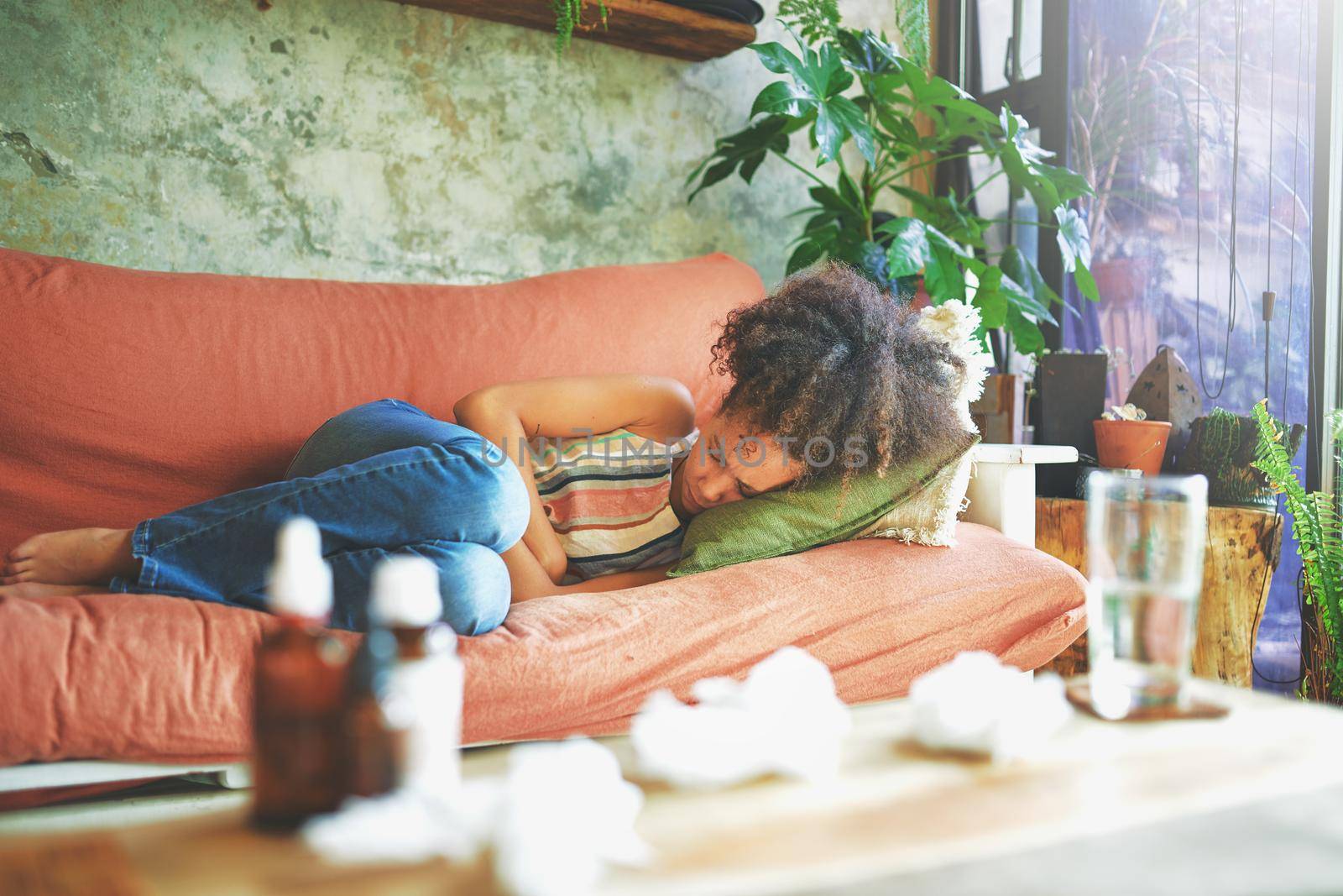 Shot of a young woman experiencing stomach pain while lying on the sofa at home stock photo