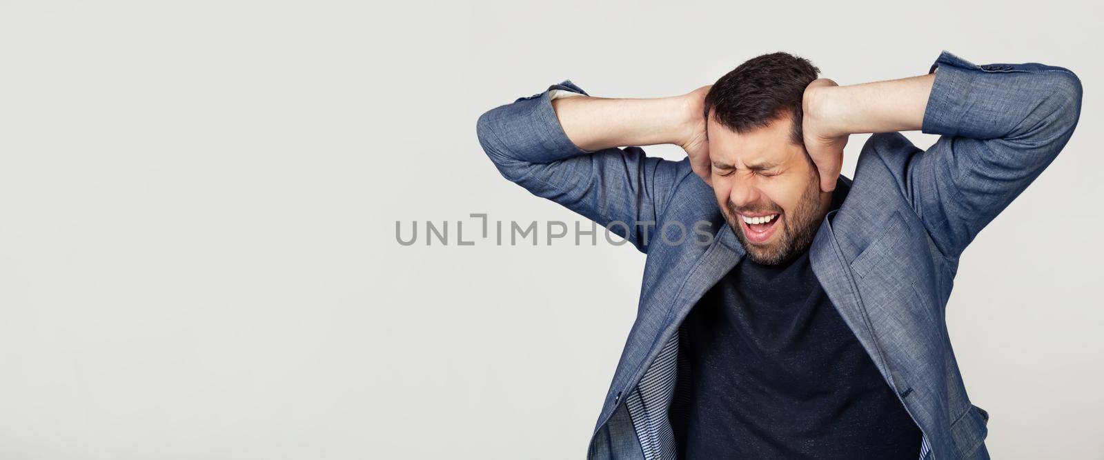 Young businessman man with a beard in a jacket. Hands on head, suffering from headache in despair and under stress due to pain and migraine. Portrait of a man on a gray background.