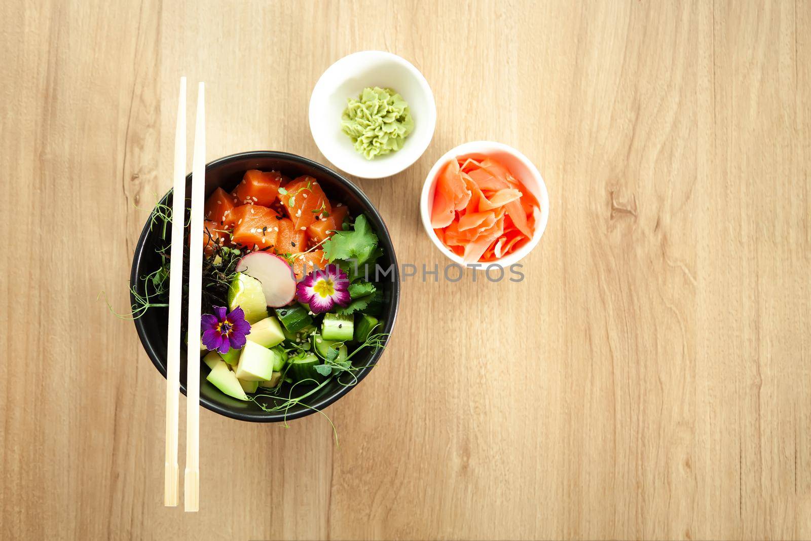 Poke salad with salmon in a bowl next to wasabi and ginger. Ingredients fresh salmon, avocado, cucumber, rice, Tamarind sauce mango sauce nori lime, sesame seeds, cilantro. Asian seafood salad concept