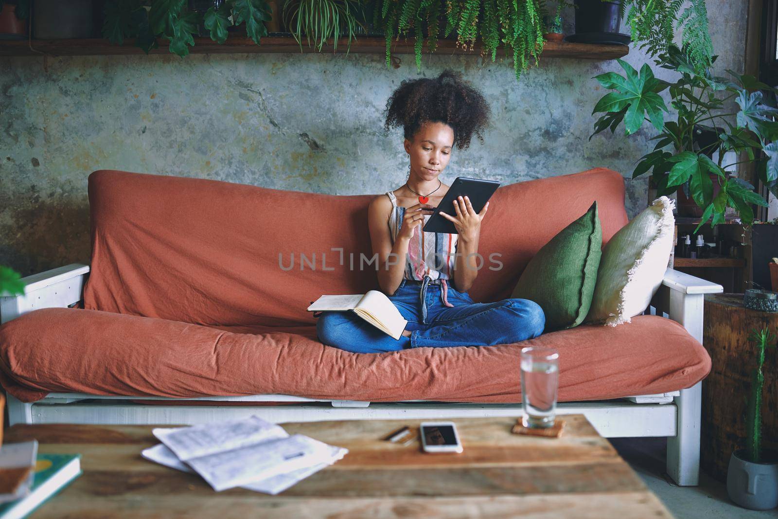 Beautiful African woman scrolling on her tablet and making notes in her living room