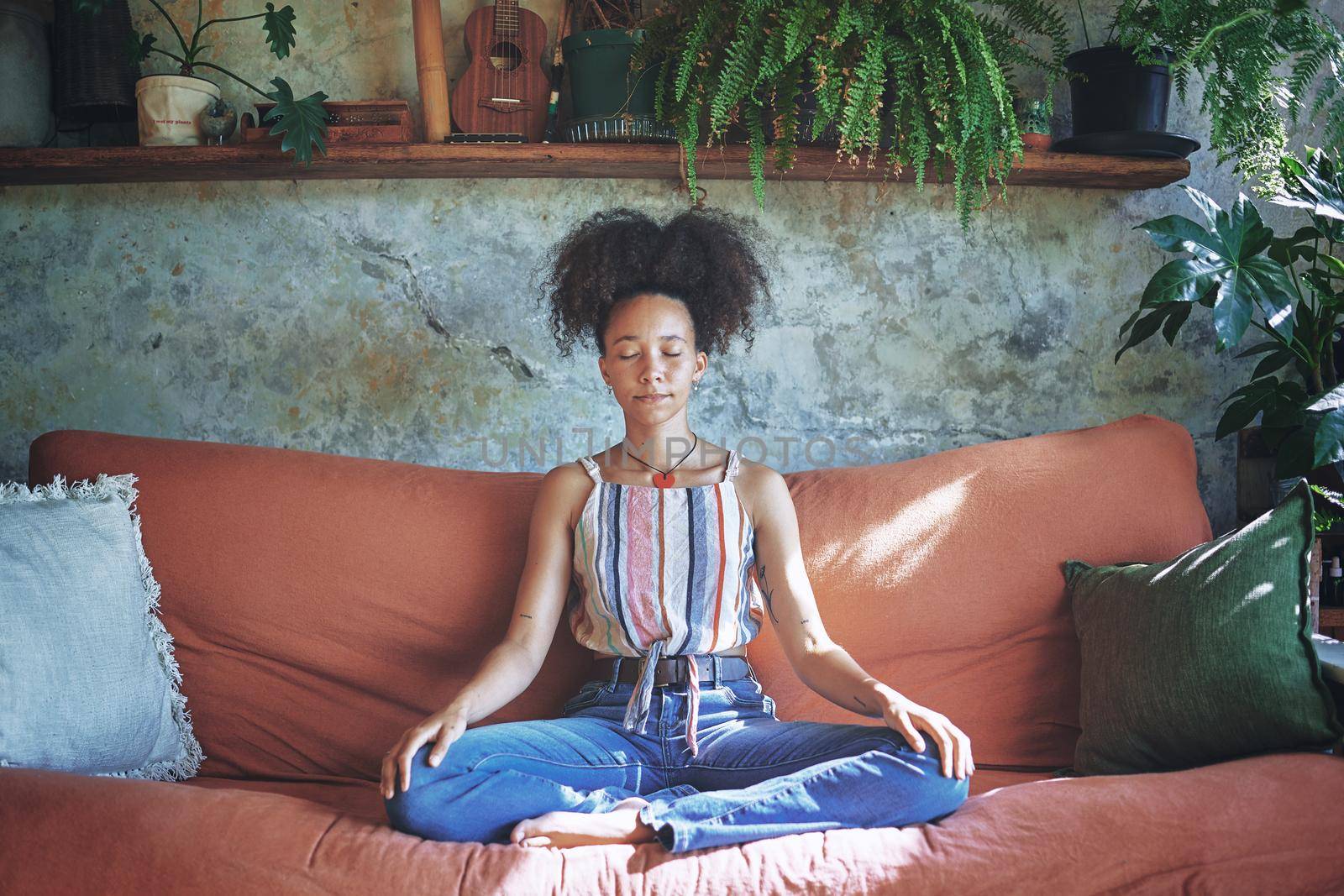 Shot of a beautiful African woman meditating on the sofa at home - Stock Photo