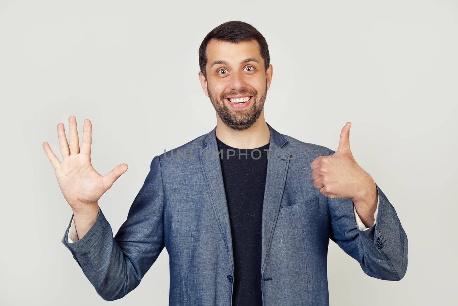 Young businessman man with beard smiling, showing number six with fingers on hand, smiling confidently and happily, looking into the camera. The man shows six fingers. Number 6.