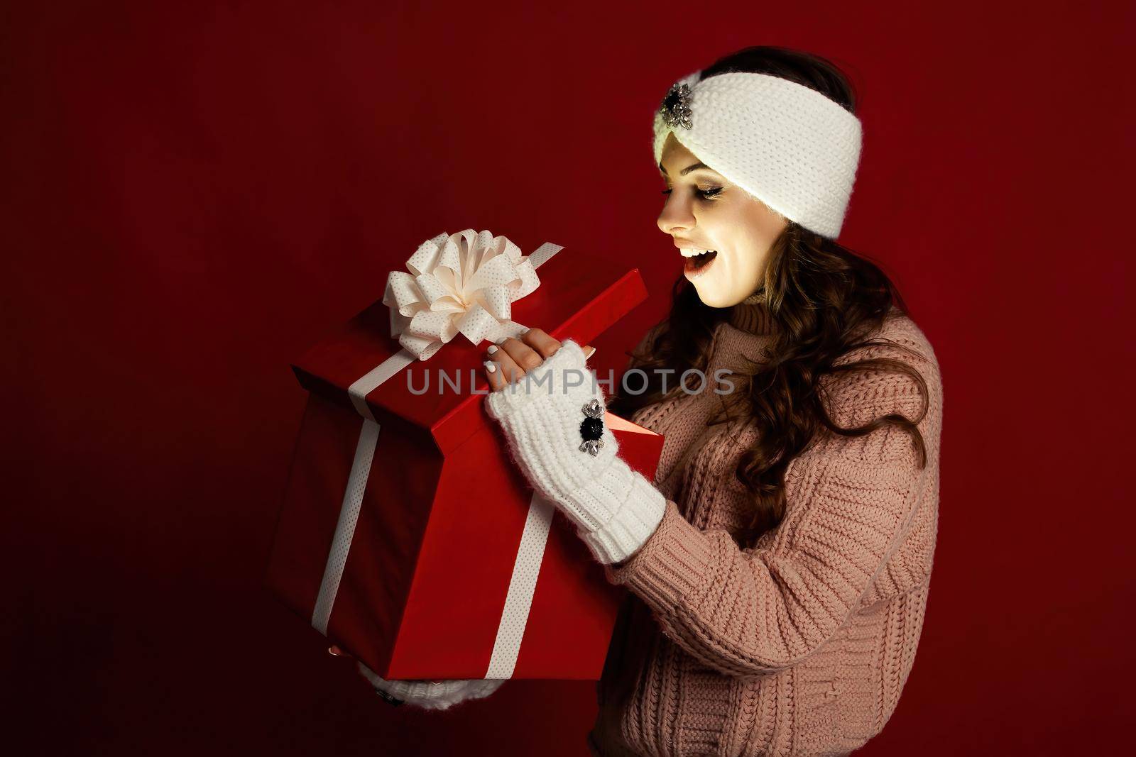 Happy young woman with a present, opening a Christmas present box. Portrait of happy smiling girl opening gift box isolated on red background