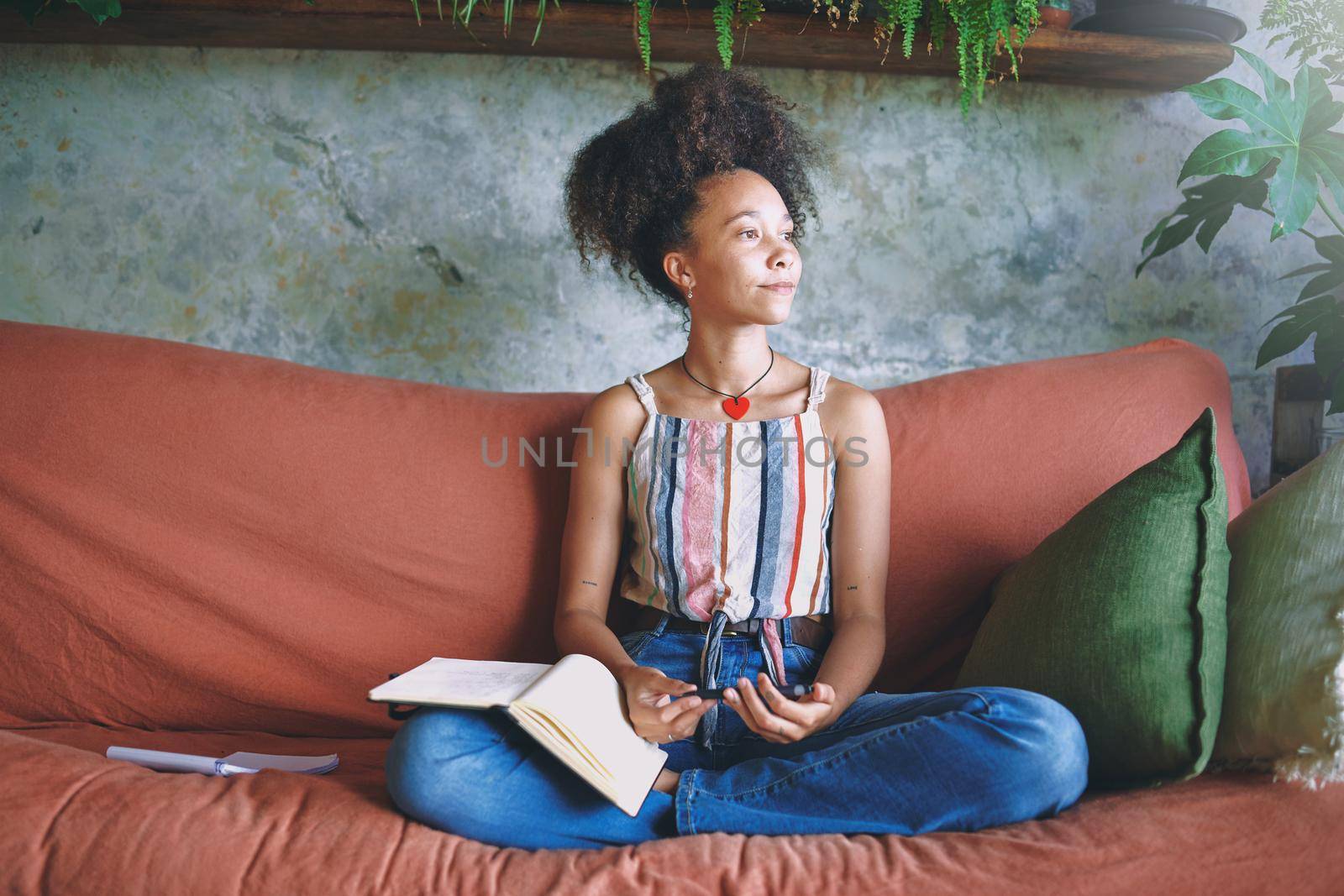 Beautiful African woman making notes while relaxing on the sofa at home stock photo