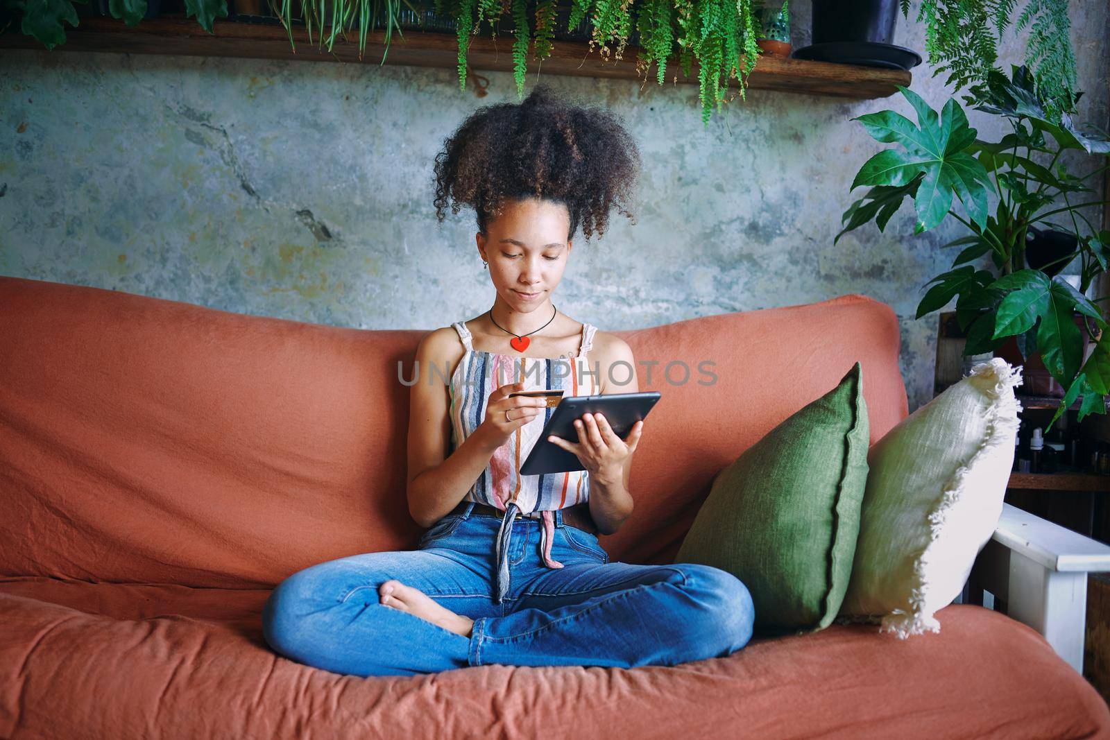 Shot of a beautiful African woman doing online banking from her sofa