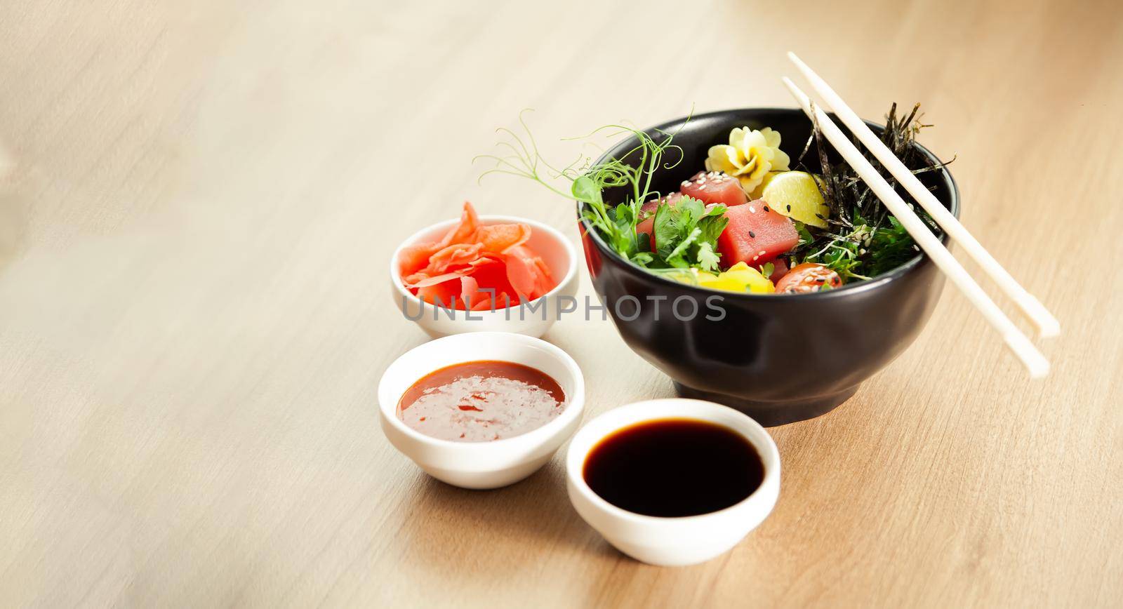 Poke salad with tuna in a bowl. Ingredients fresh tuna, cherry tomatoes, marinated seaweed, rice, takuan, Ponzu sauce, Teriyaki sauce, nori, sesame seeds, lime, cilantro. Asian seafood salad concept