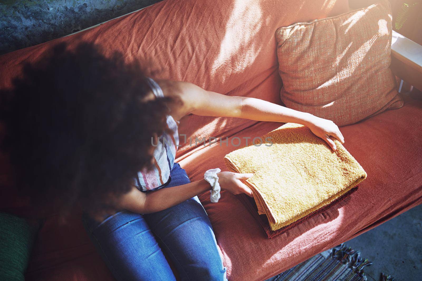 Shot of a beautiful African woman folding washed laundry while sitting on her couch - Stock Photo