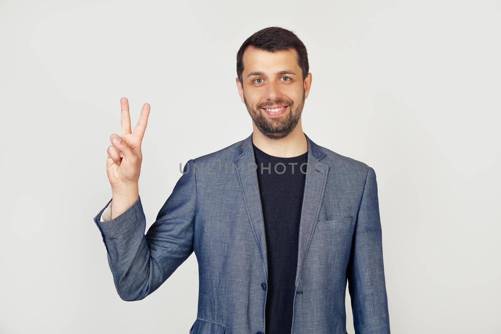 Young businessman man with beard smiling, showing number two with fingers on hand, smiling confidently and happily, looking into the camera. The man shows two fingers. Number 2.